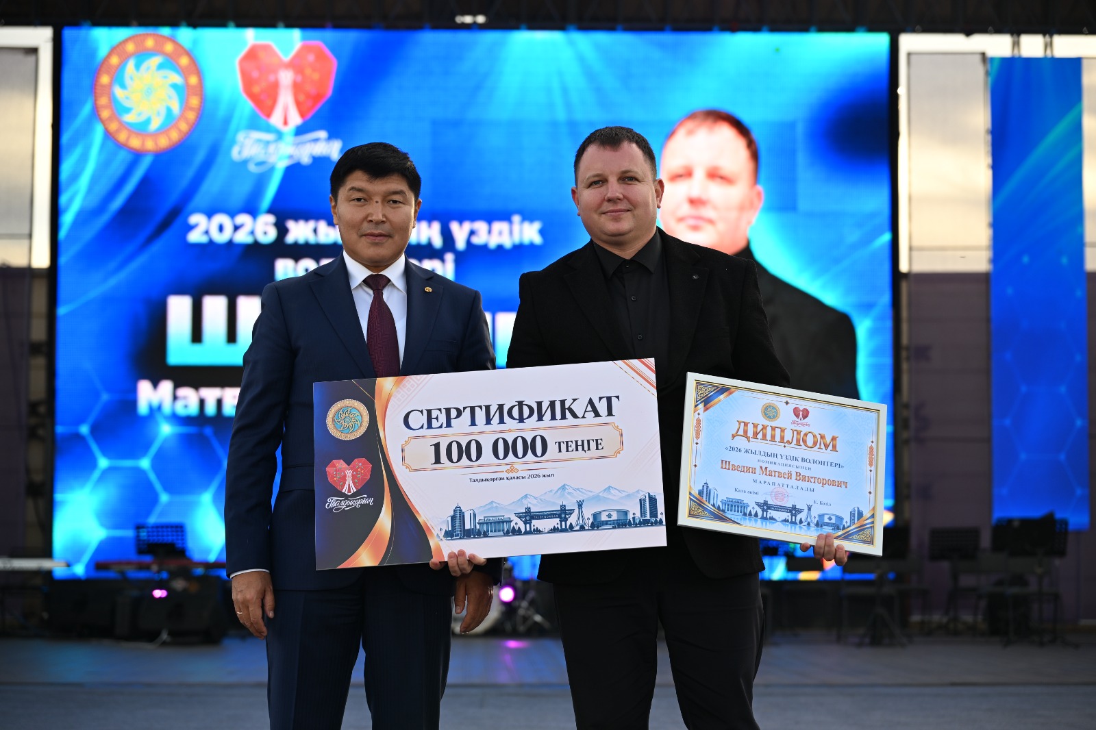 Екі ер адамның сертификат пен диплом ұстап тұрған суреті.
