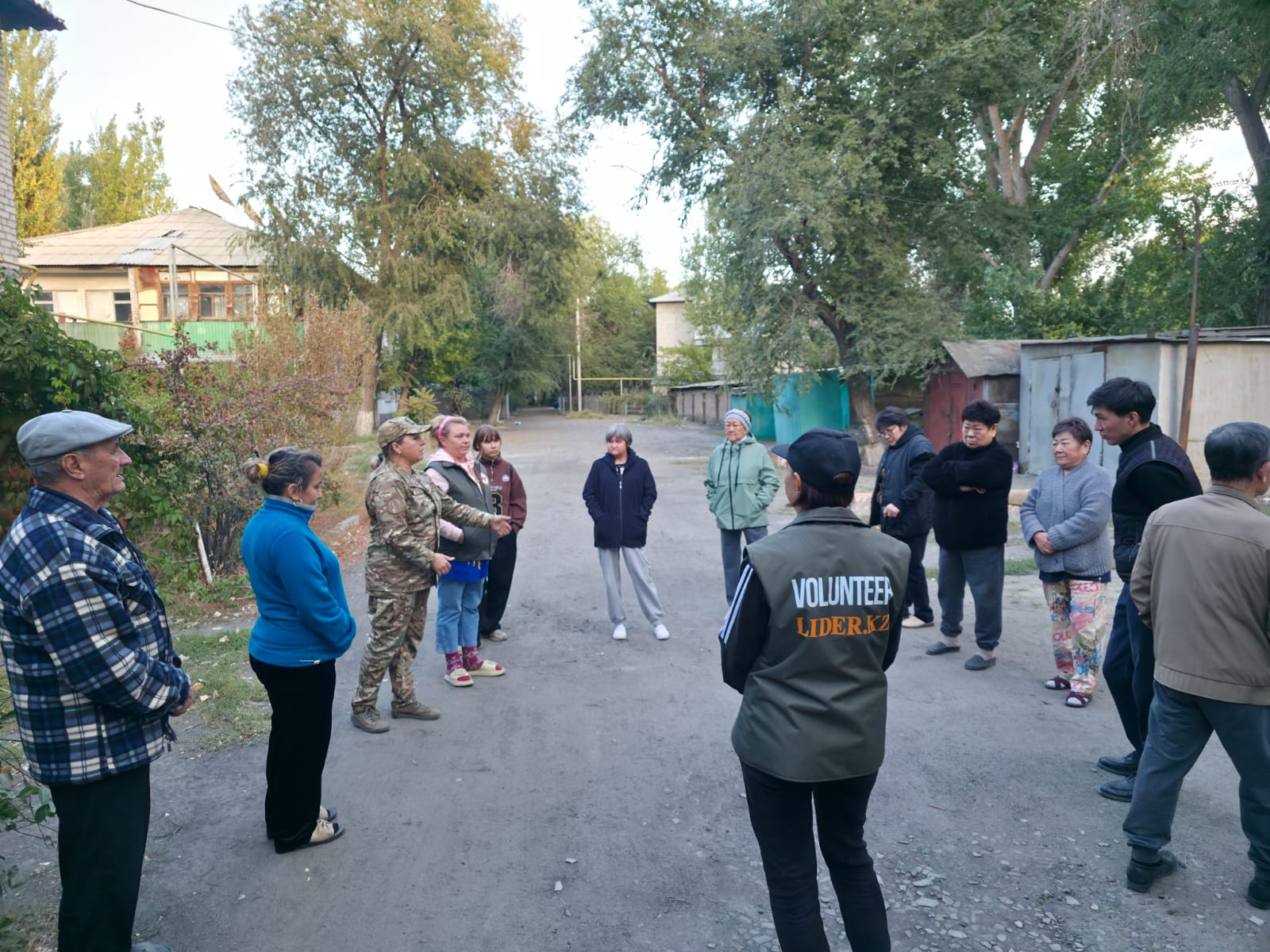 Группа людей, включая волонтера и женщину в камуфляже, общается на улице в сельской местности.