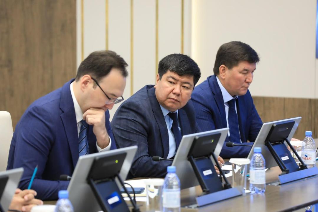 Жиналыста отырған костюм киген үш ер адам.