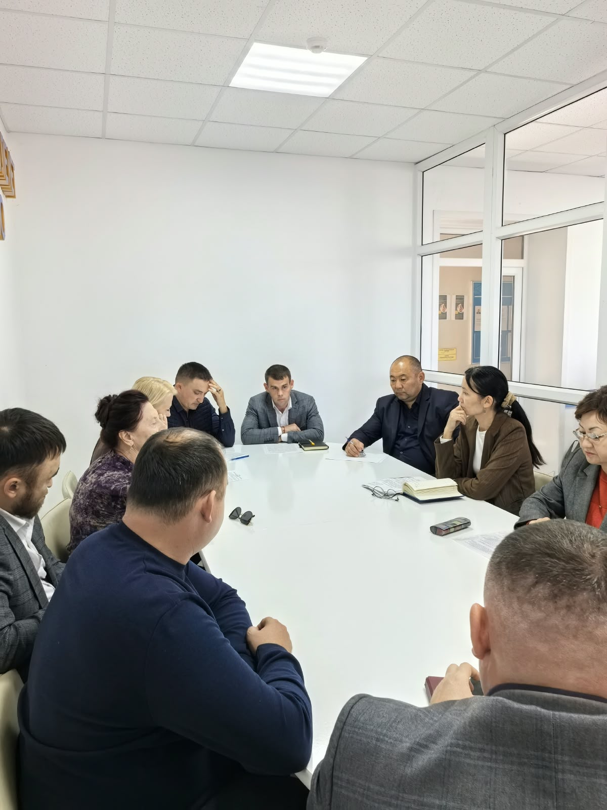 Ақ үстелдің төңірегінде жиналып, кеңес beszіп отырған адамдар тобы.