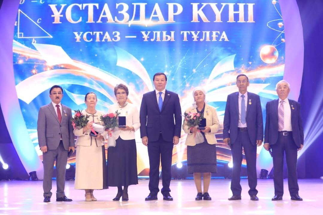 «Ұстаздар күні» мерекесінде сыйлық алған мұғалімдер мен қонақтардың сахнадағы топтық суреті.