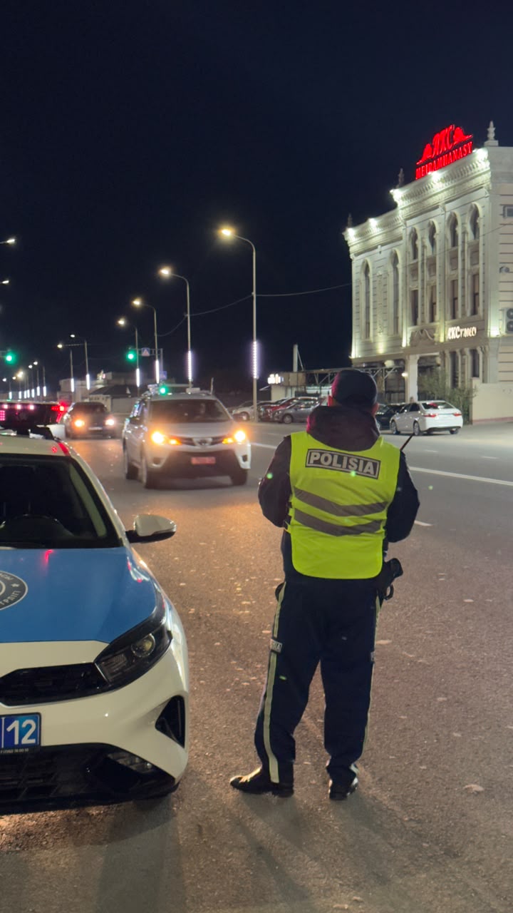 Түнгі қалада жол жиегінде тұрған полиция қызметкері және патрульдік көлік.