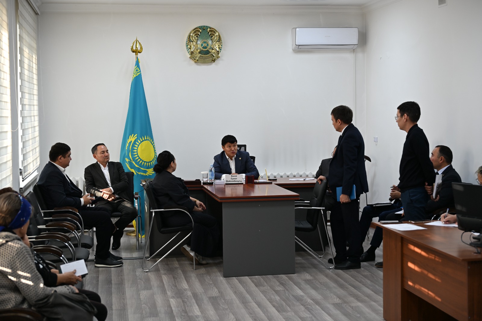 Қазақстан Республикасының мемлекеттік рәміздері бар кеңседе өткізіліп жатқан ресми жиналыс.