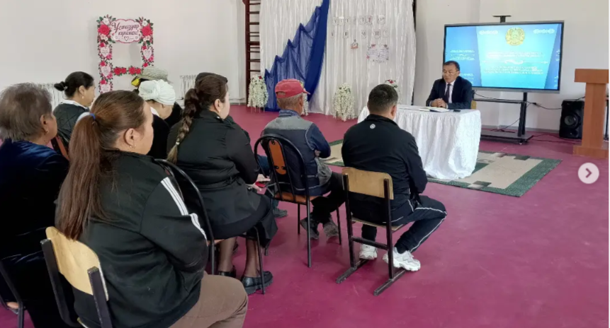 Экран алдында баяндама жасап жатқан әкім және оны тыңдап отырған адамдар.