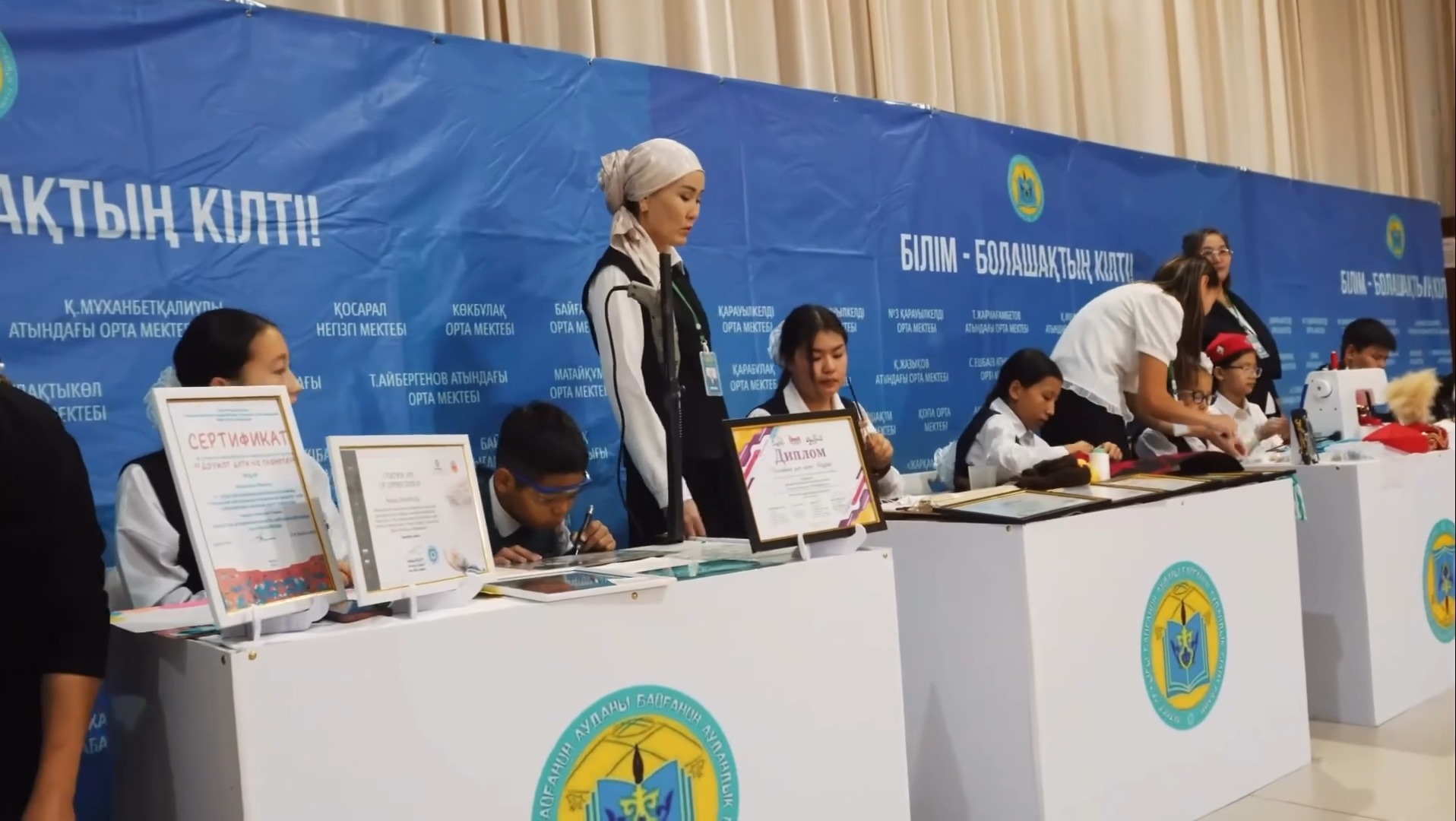 «Білім – болашақтың кілті» іс-шарасындағы сертификаттар мен дипломдар тұрған тіркеу үстелдері мен қатысушылар.