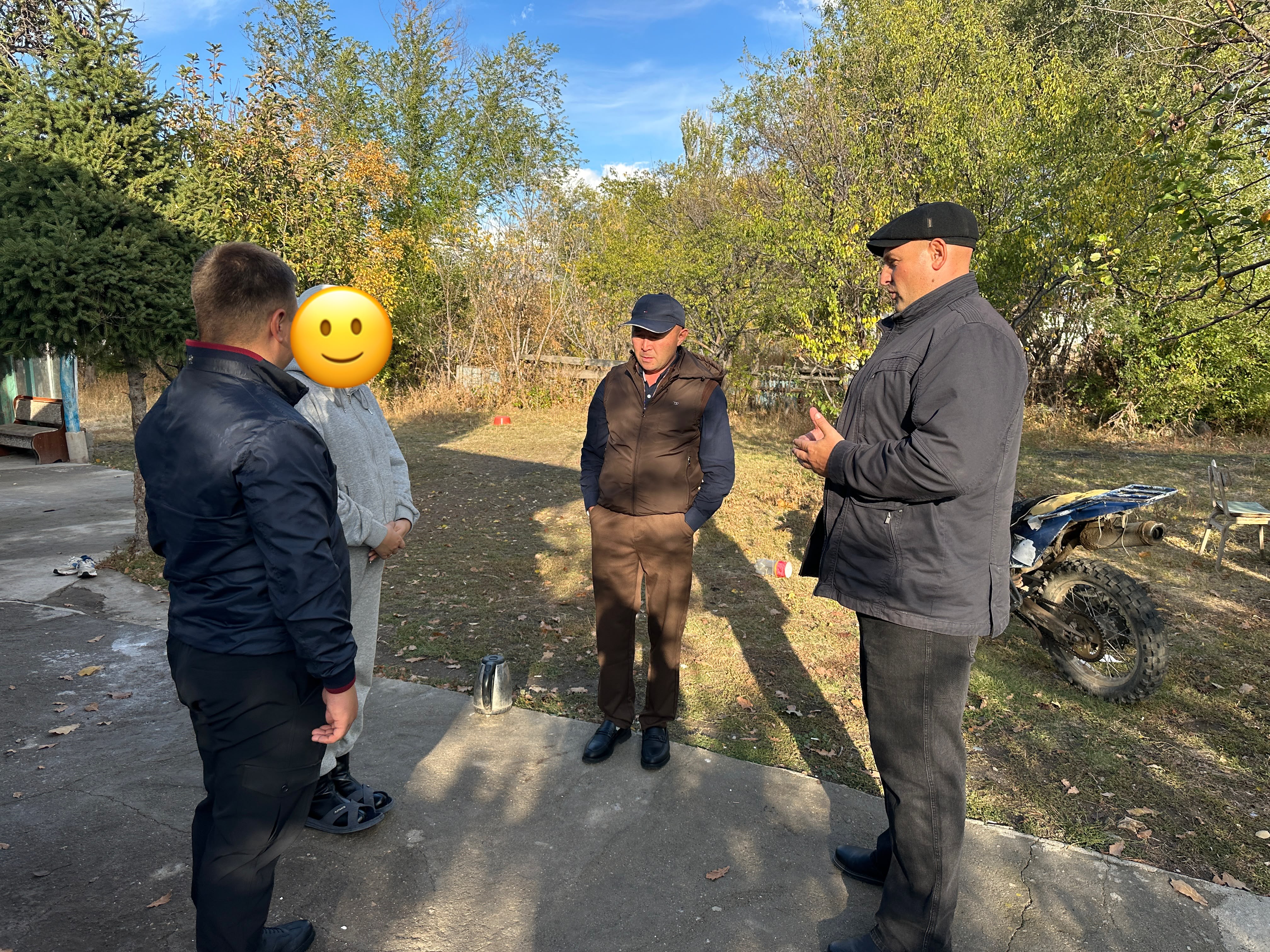Группа мужчин разговаривает на улице на фоне деревьев.