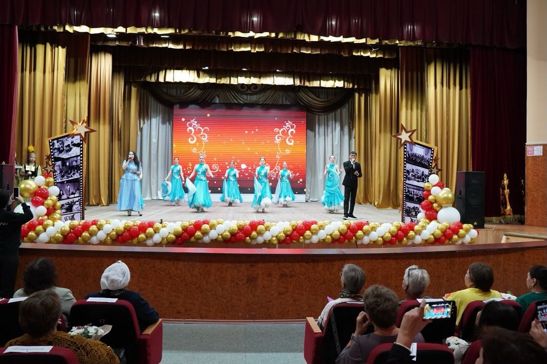 Көк көйлек киген бишілер мен жүргізушінің сахнадағы қойылымы.