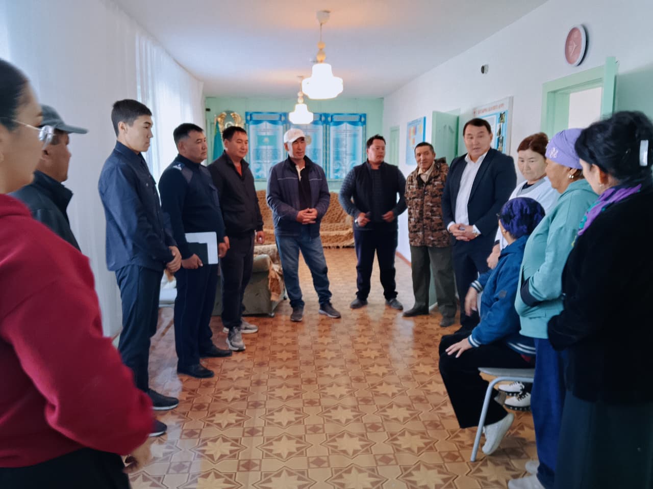 Бөлмеде жиналып, әңгімелесіп тұрған адамдар тобы.