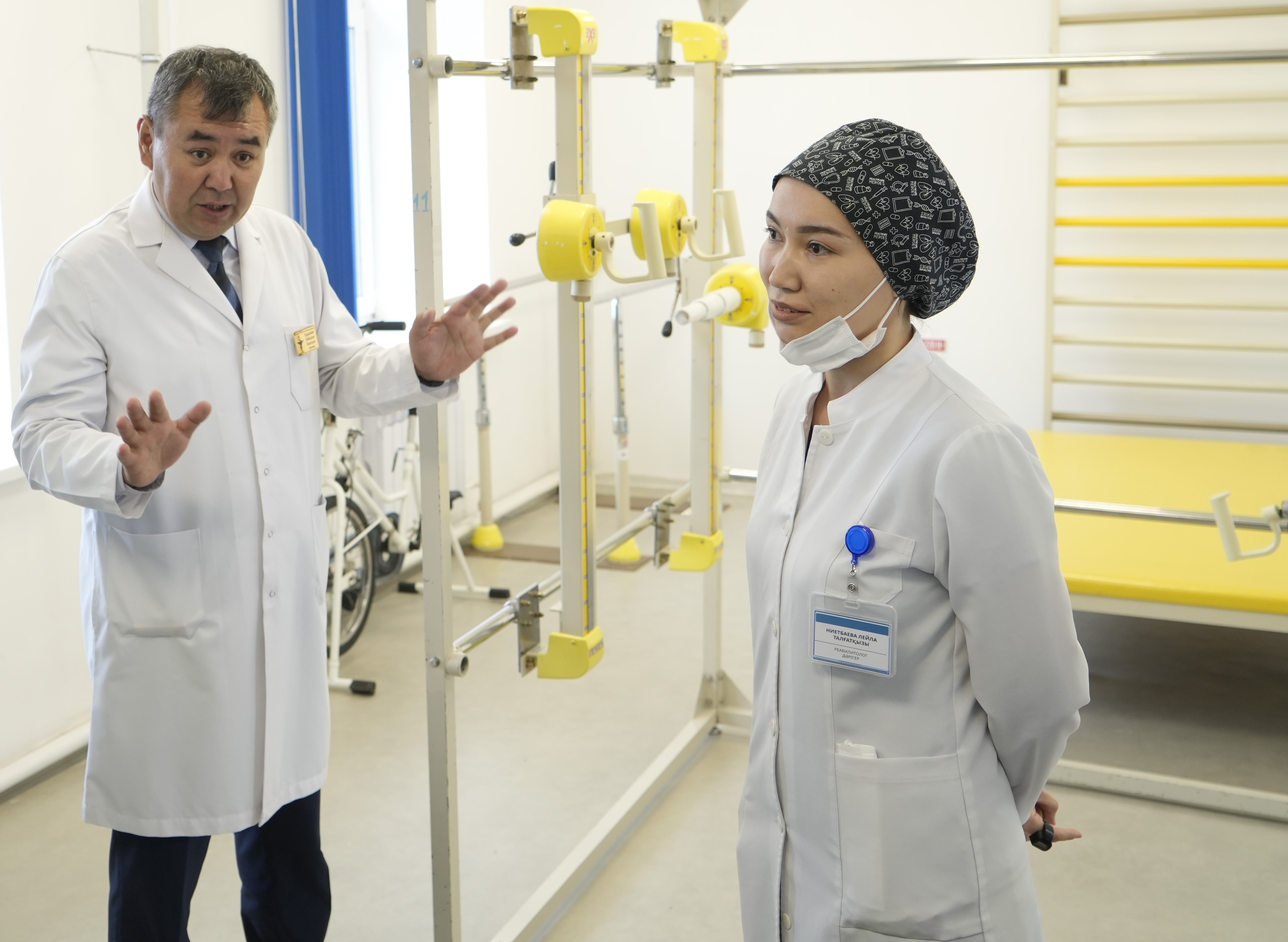 Оқу залындағы медициналық жабдықтар жанында тұрған дәрігер мен медбике.