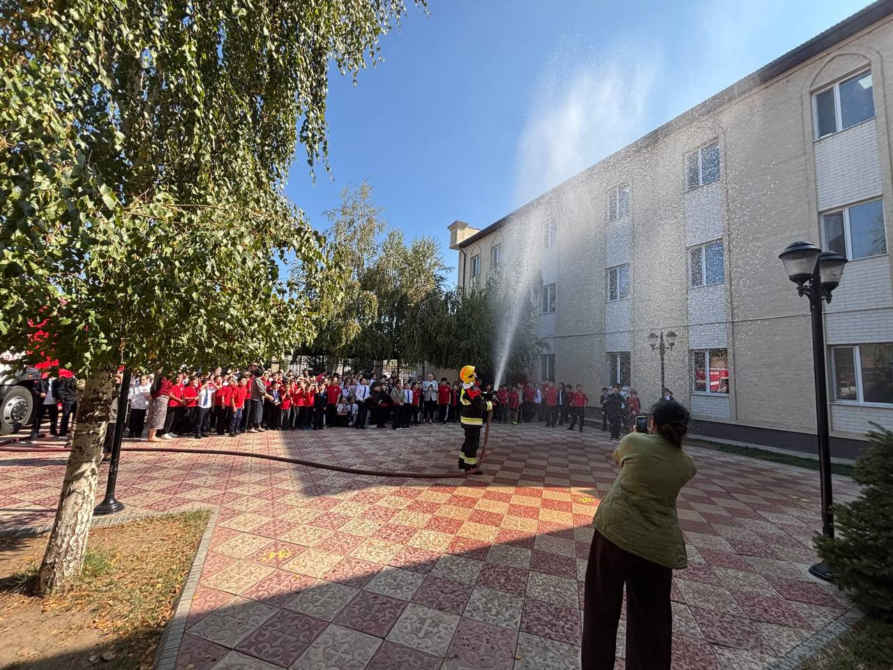 Өрт сөндірушінің балалар жинаған алаңда су шашып көрсетіп жатқан сәті.