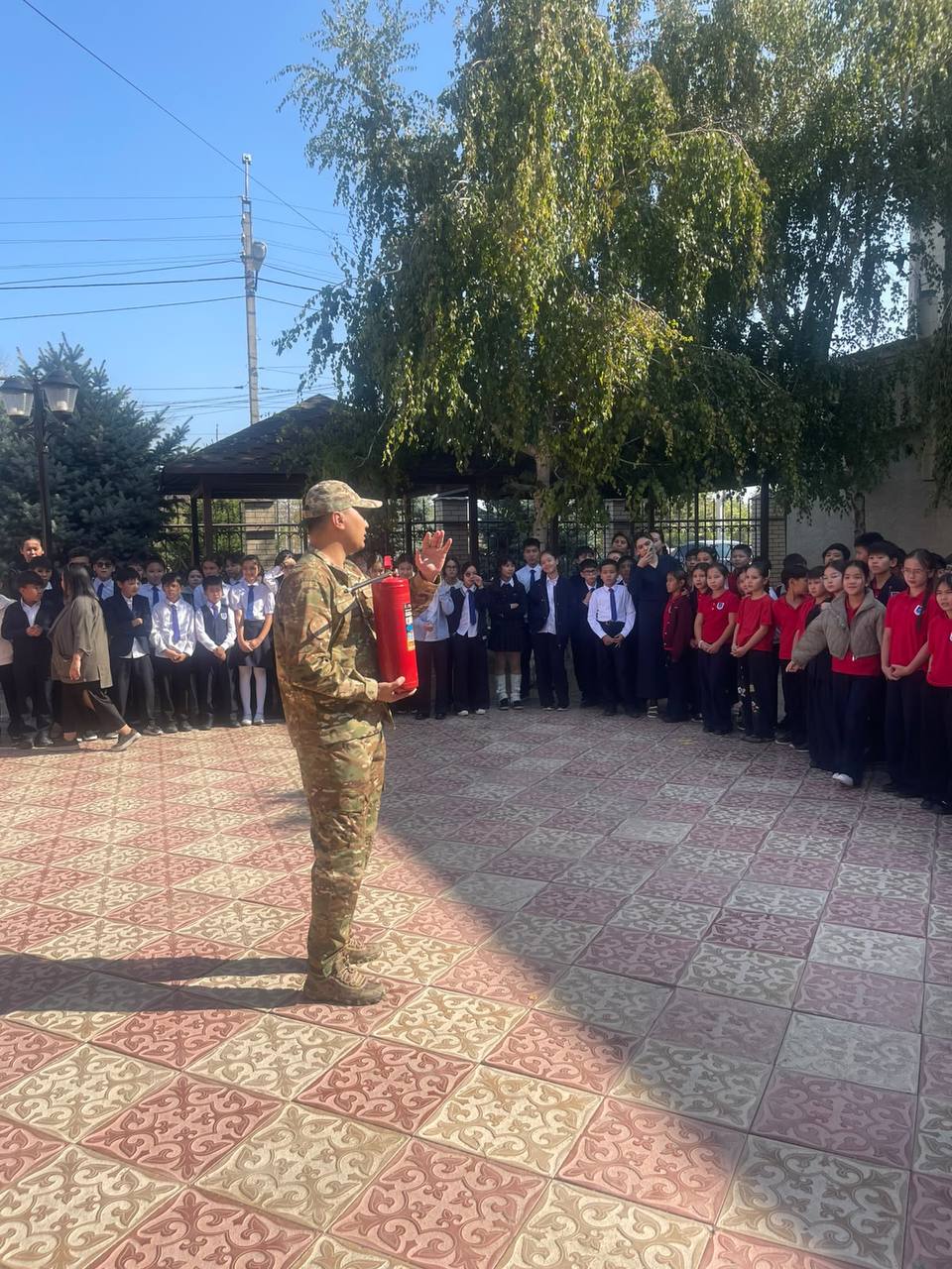 Әскери формадағы маман мектеп оқушыларына өрт сөндіруіш құрылғыны қолдану бойынша нұсқаулық өткізіп жатыр.