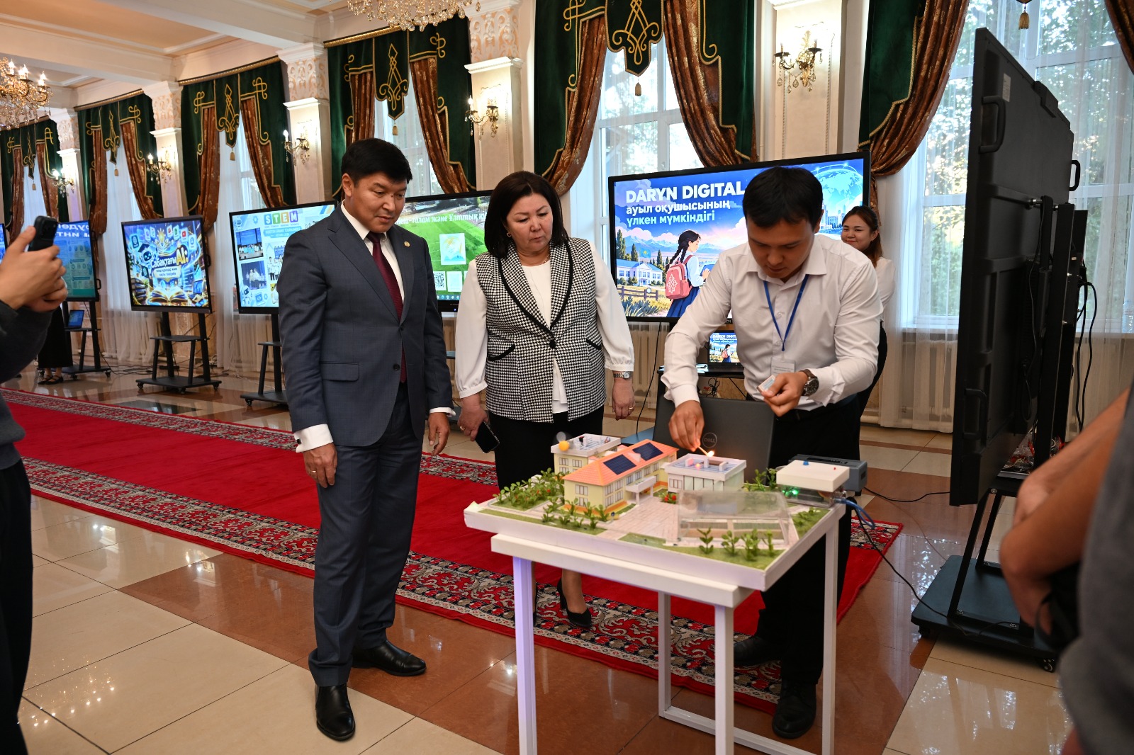 Кісілердің цифрлық жобаның макетін және мониторлардағы презентацияларды қарап тұрғаны.