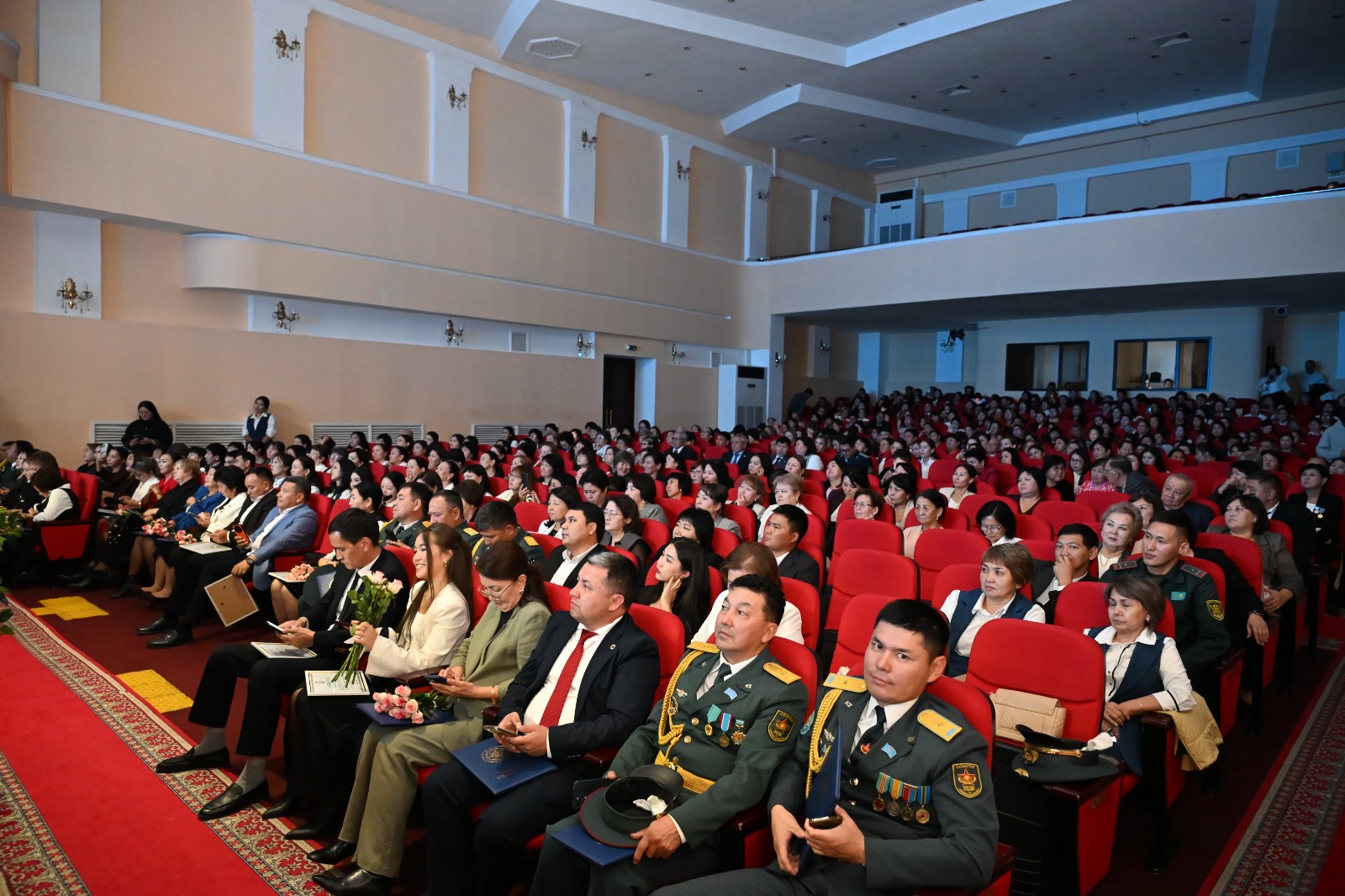 Актолдың қызыл орындықтарында отырған әскери және азаматтық киімдегі адамдар тобы.