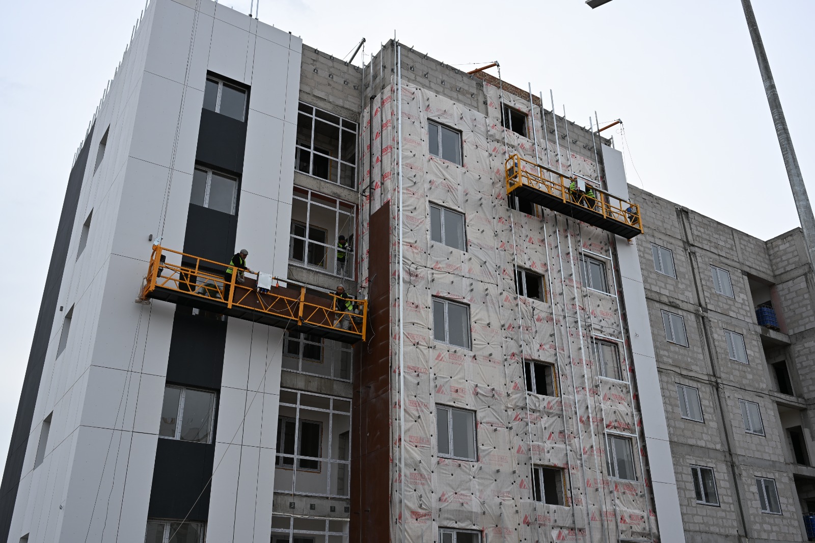 Құрылыс кезеңіндегі көпқабатты ғимарат және сыртқы қабырғасын жөндеп жатқан жұмысшылар.
