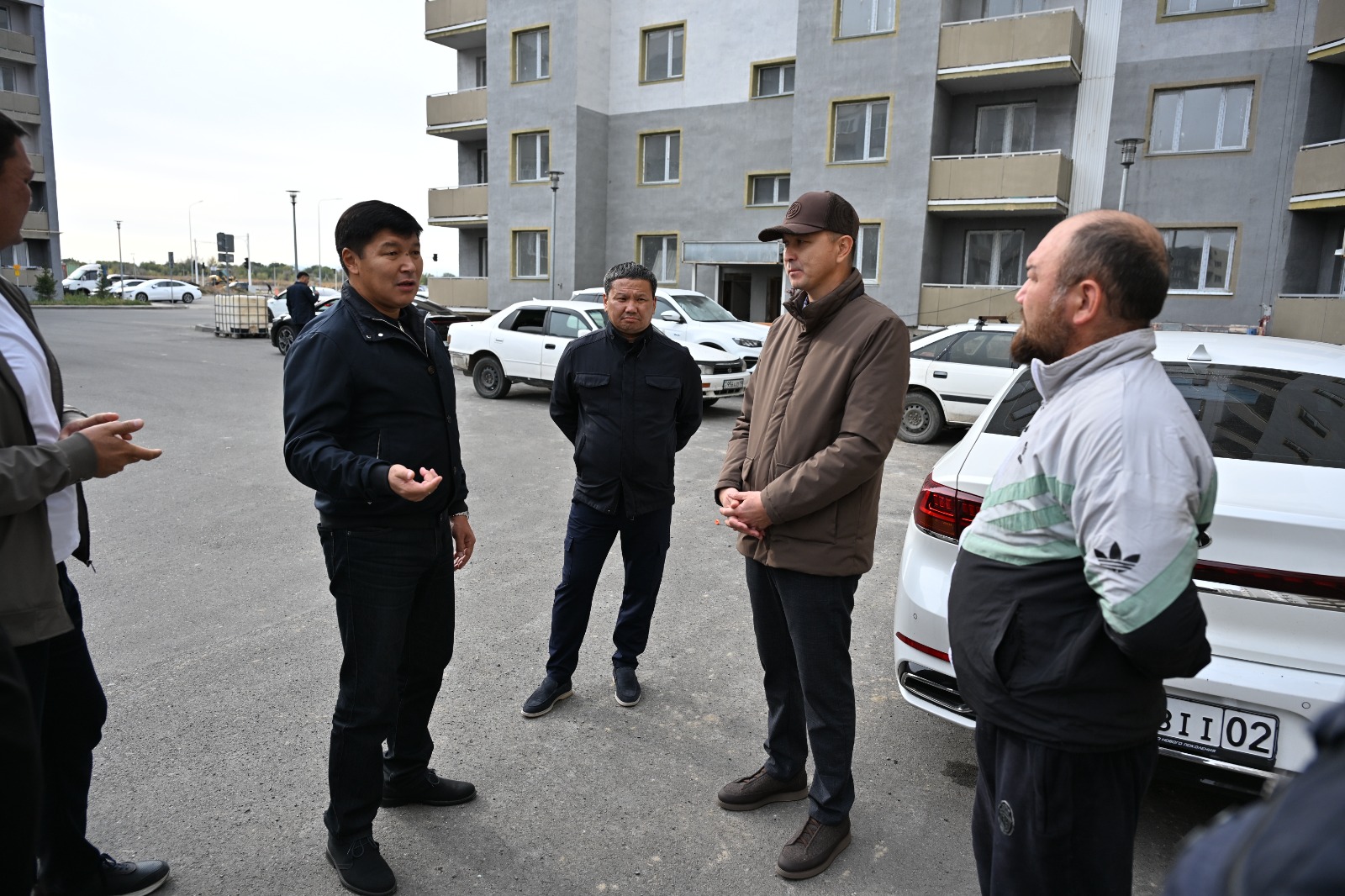 Көппәртаулы үйдің алдында тұрып, әңгімелесіп жатқан ер адамдар тобы.