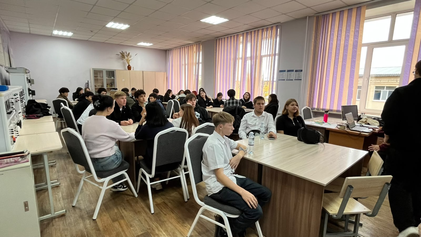 Сыныпта үстел басында отырған студенттер тобы және алдында тұрған мұғалім.