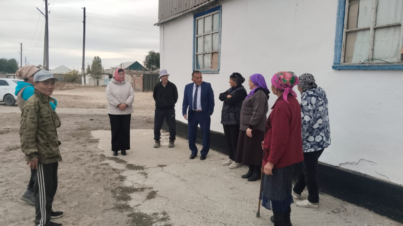 Ақ үйдің алдында жиналған адамдар тобы және костюм киген ер адам.