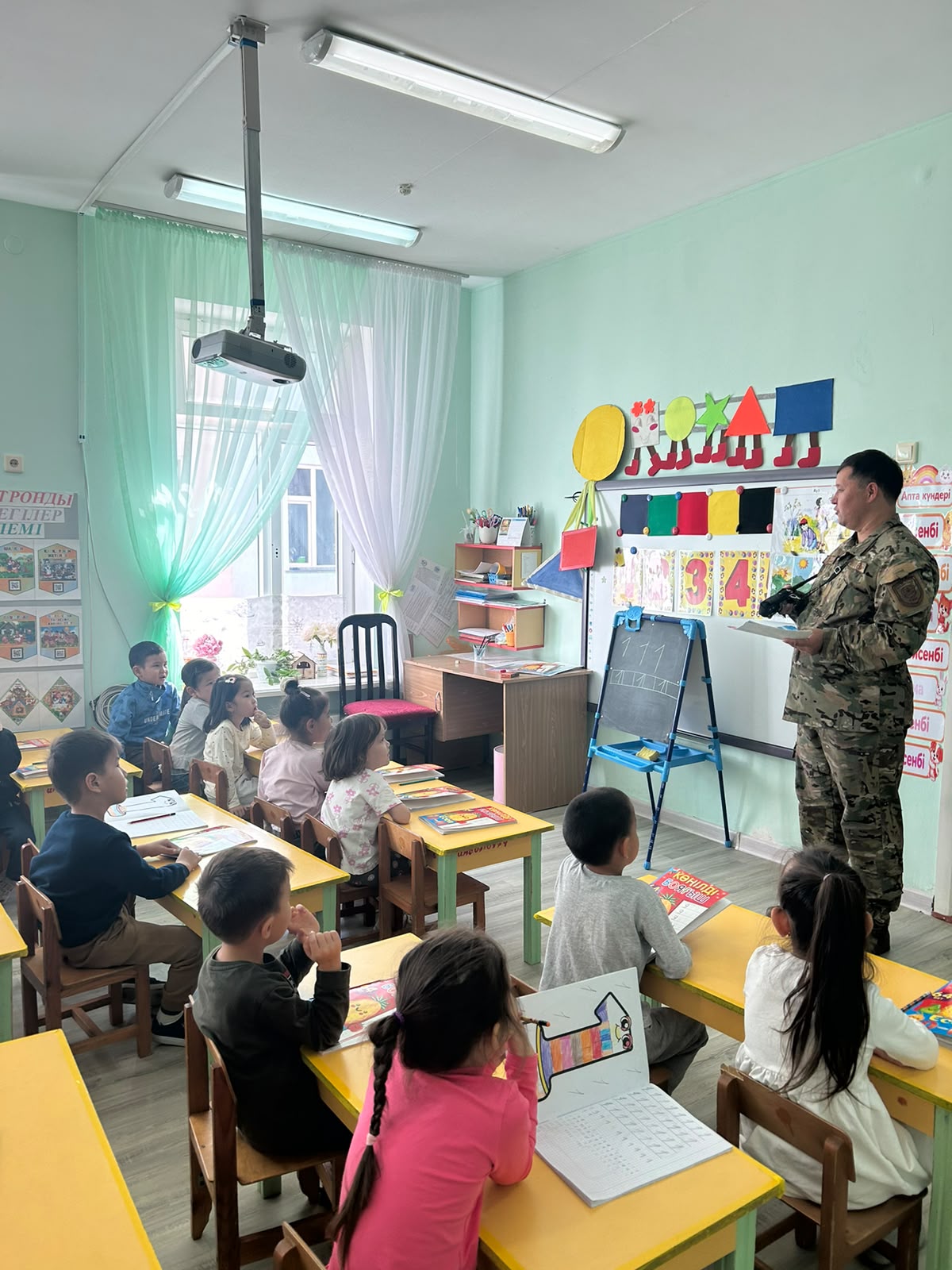 Военный в камуфляже проводит урок в классе с маленькими детьми.