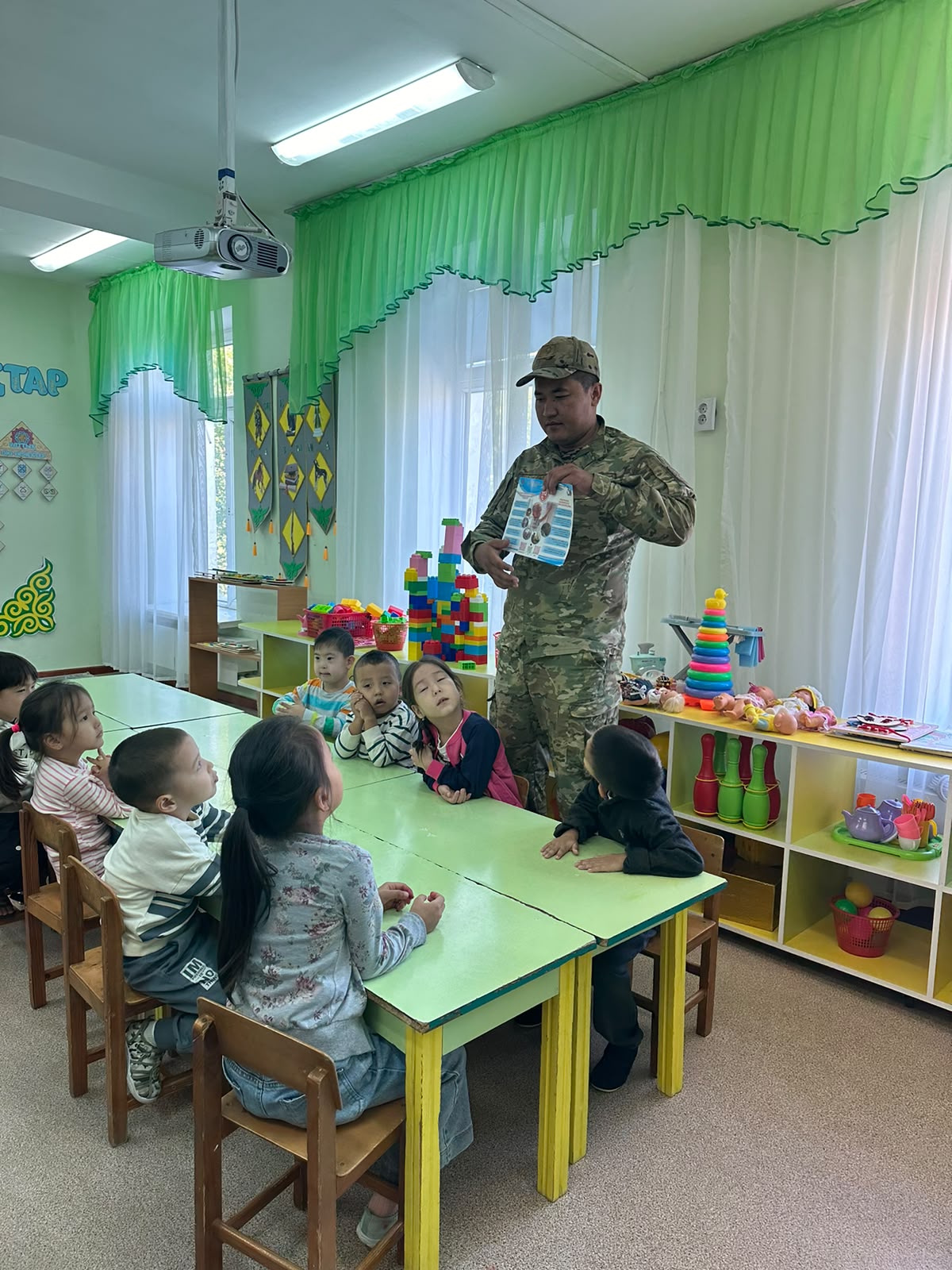 Военный в камуфляже показывает книгу детям в детском саду.