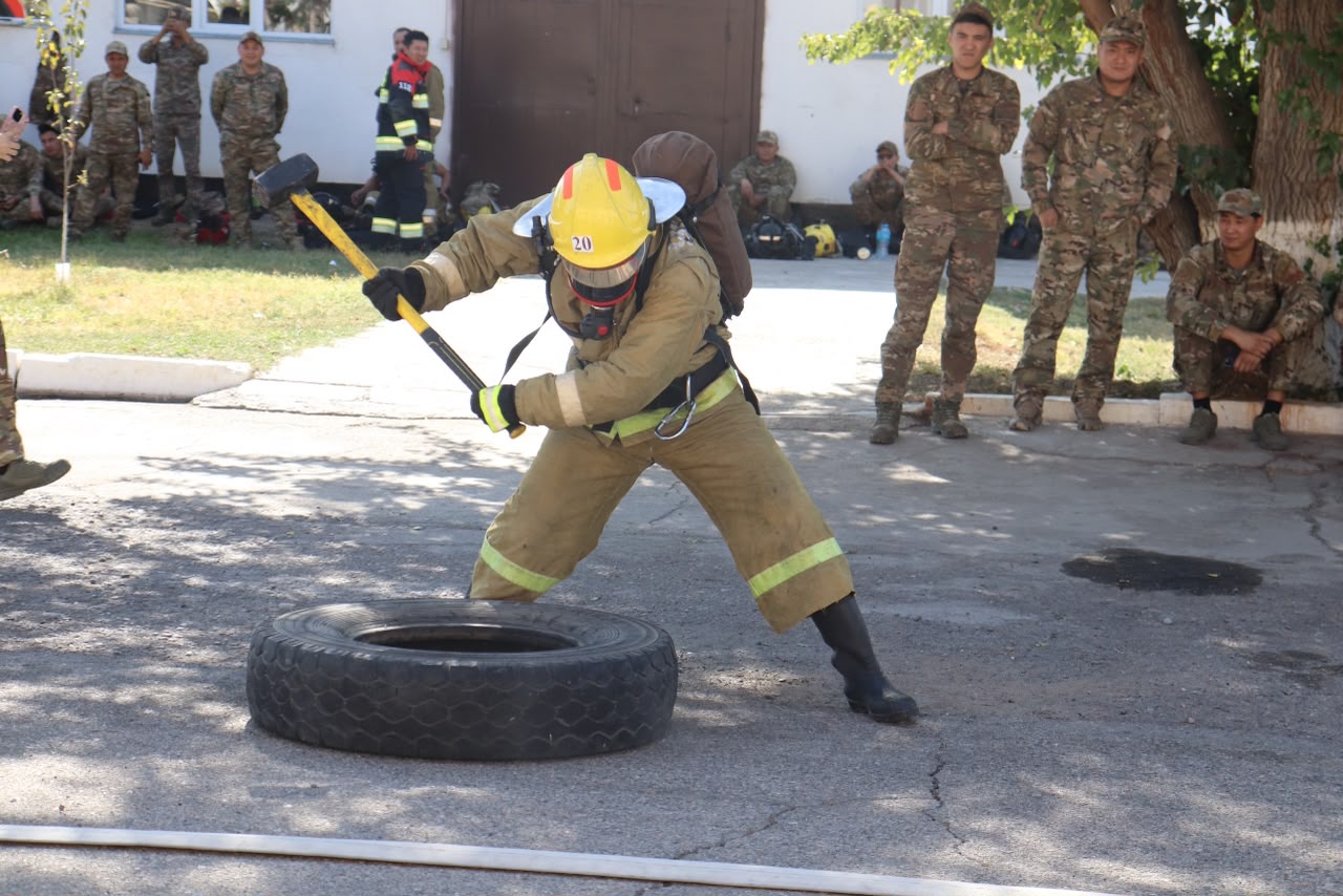 Өрт сөндірушінің арнайы киімде дөңгелекке балғамен соғып жатқан сәті.