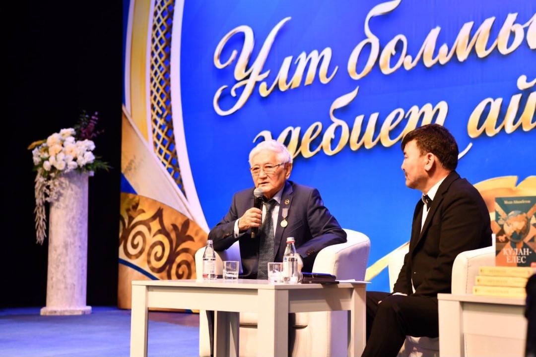 Көк фонды сахнада екі ер адамның сұхбаттасып отырғаны.