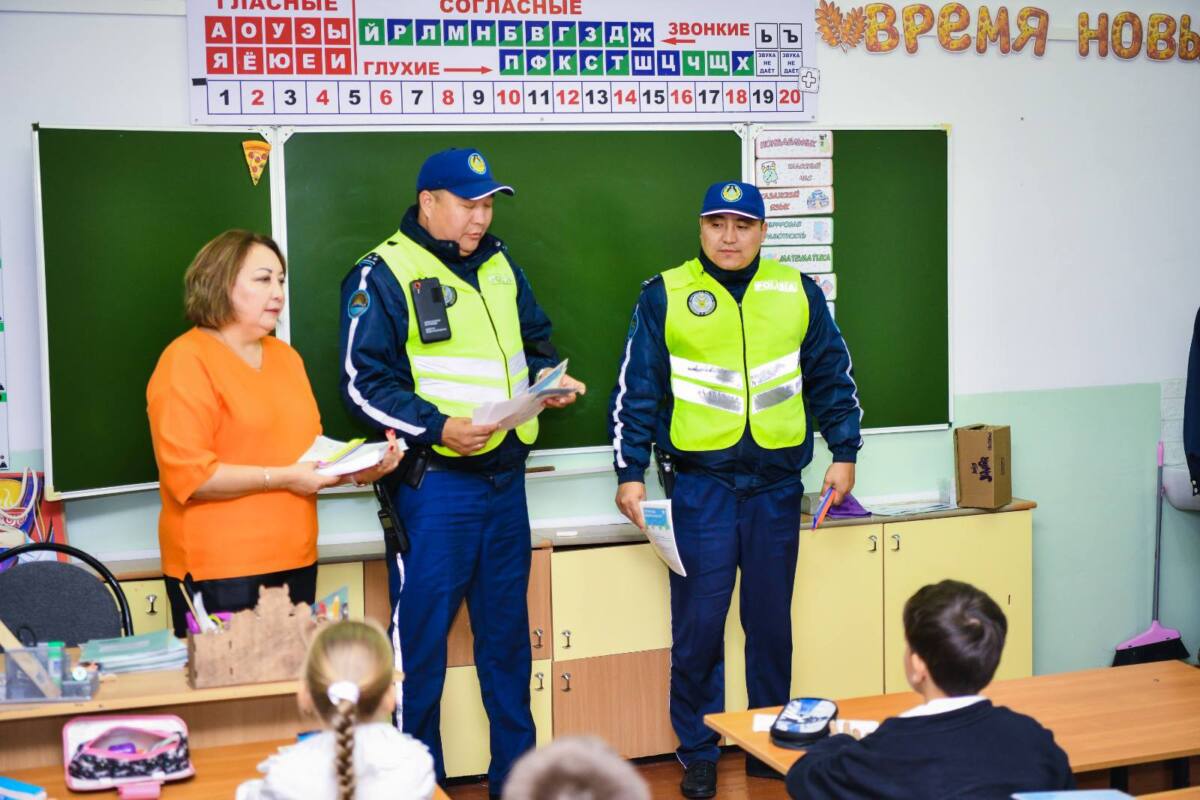 Сыныпта оқушылар алдында тұрған екі полиция қызметкері және мұғалім.