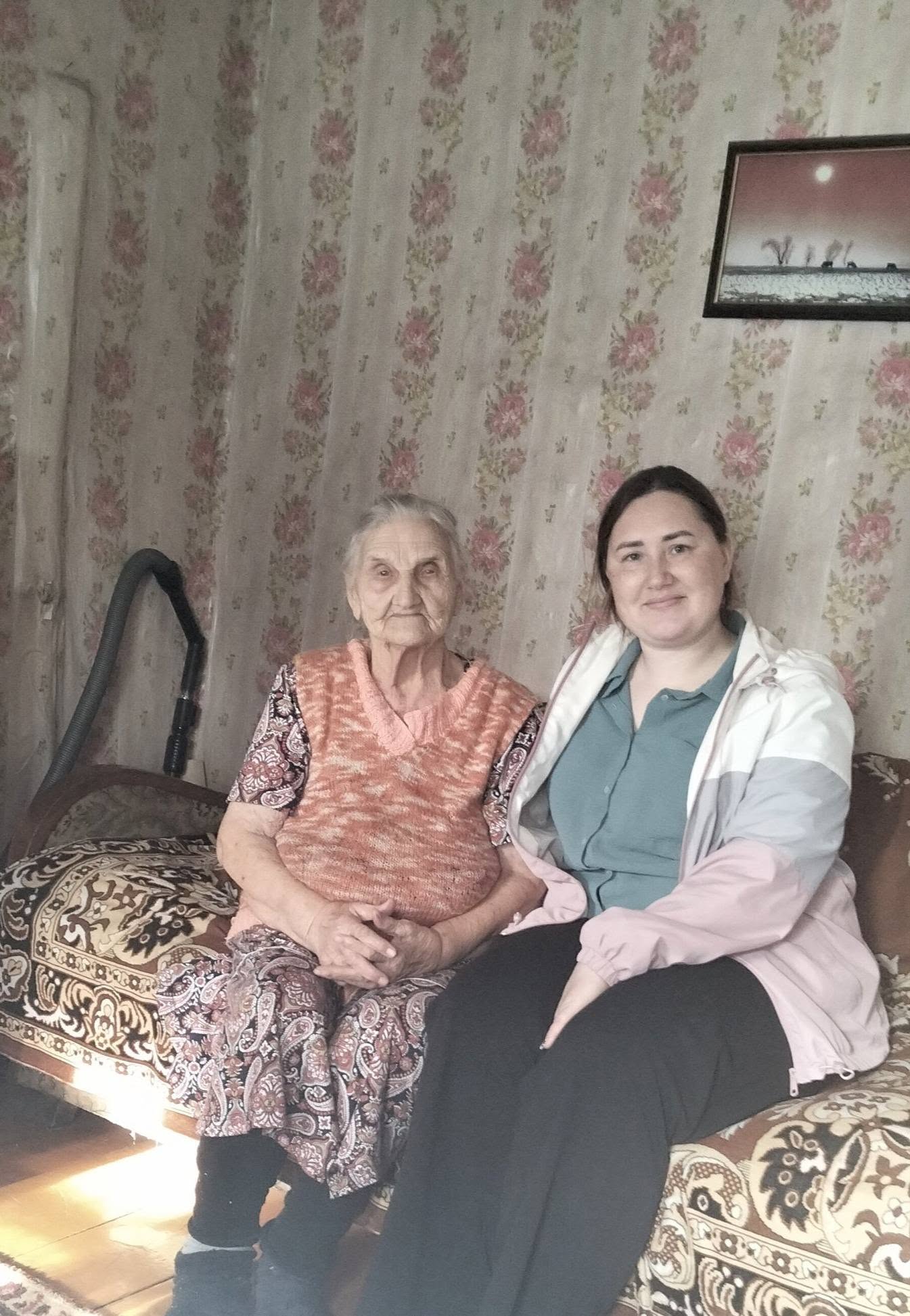 Диванда отырған қарт әже мен жас әйелдің бірге түсірілген суреті.