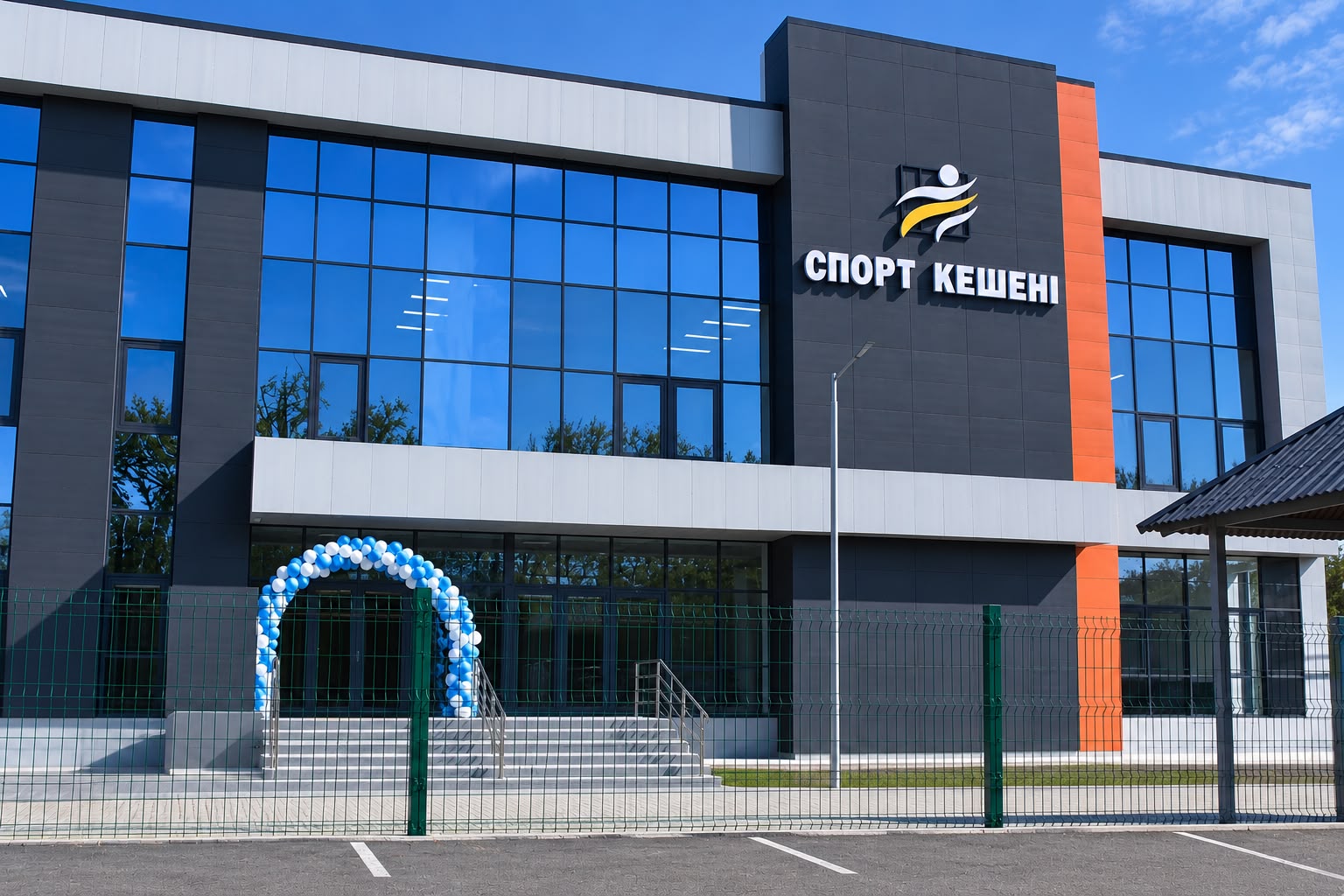 Современное здание спортивного комплекса «Спорт кешені» с панорамными окнами и аркой из сине-белых шаров у входа.