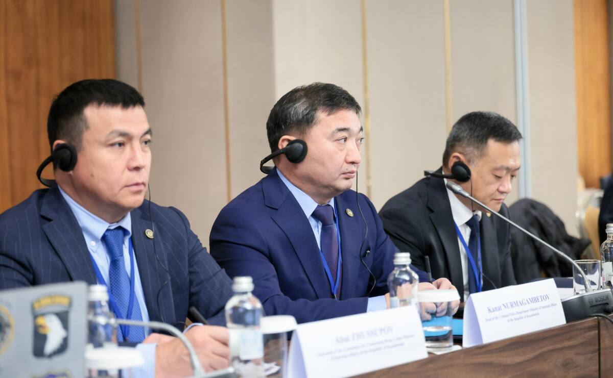 Құлаққап таққан, костюм киген үш ер адам жиналыста отыр.
