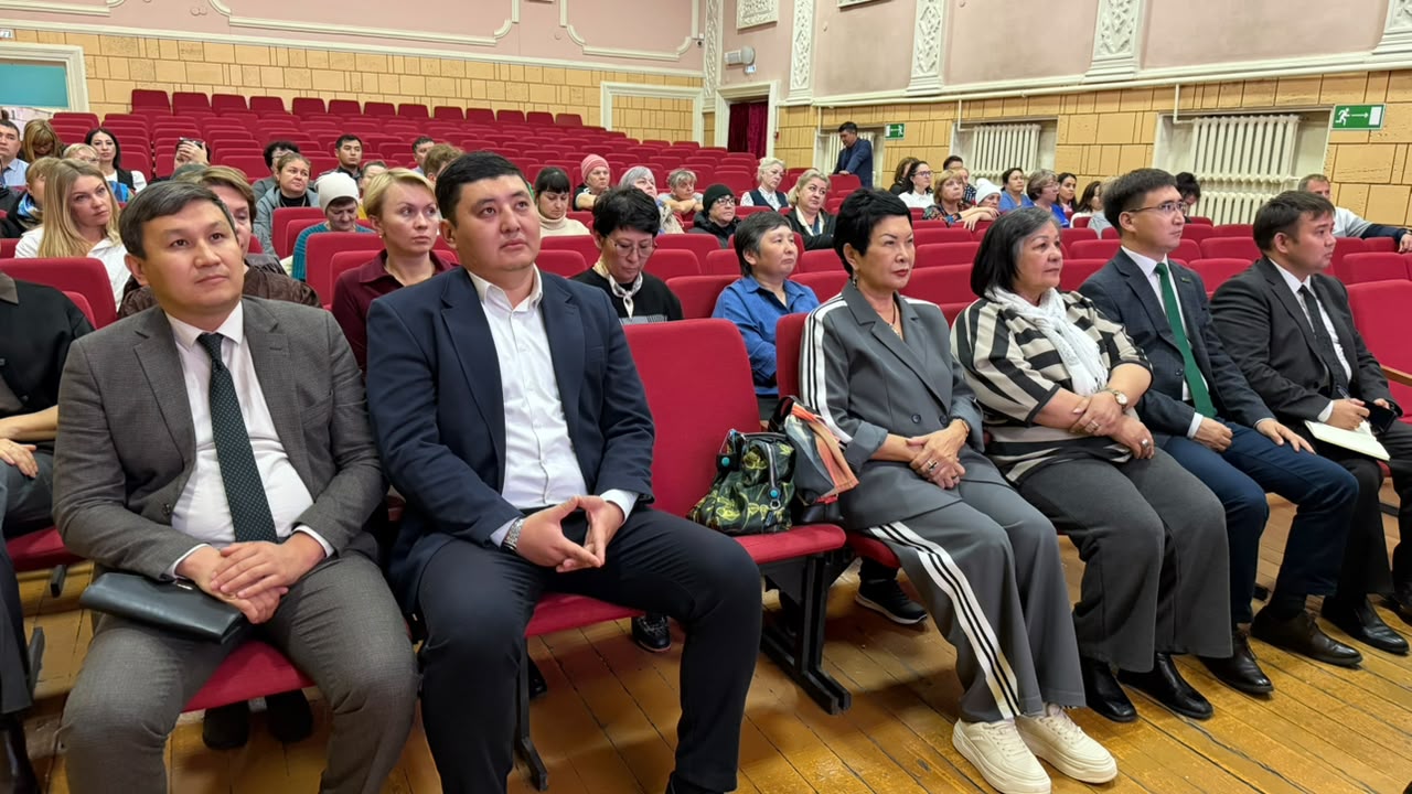 Конференция залында отырған костюм киген адамдар тобы.