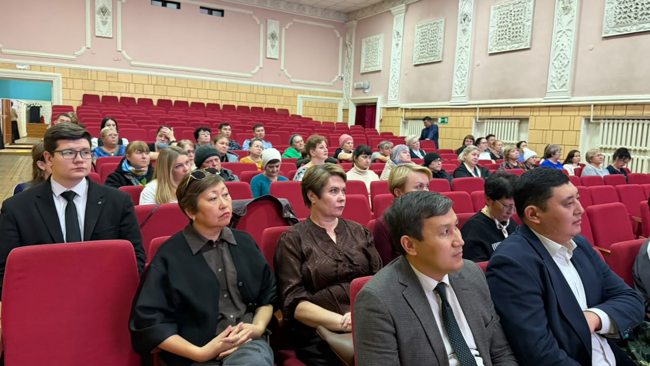 Қызыл орындықтары бар залда отырған тыңдаушылар тобы.
