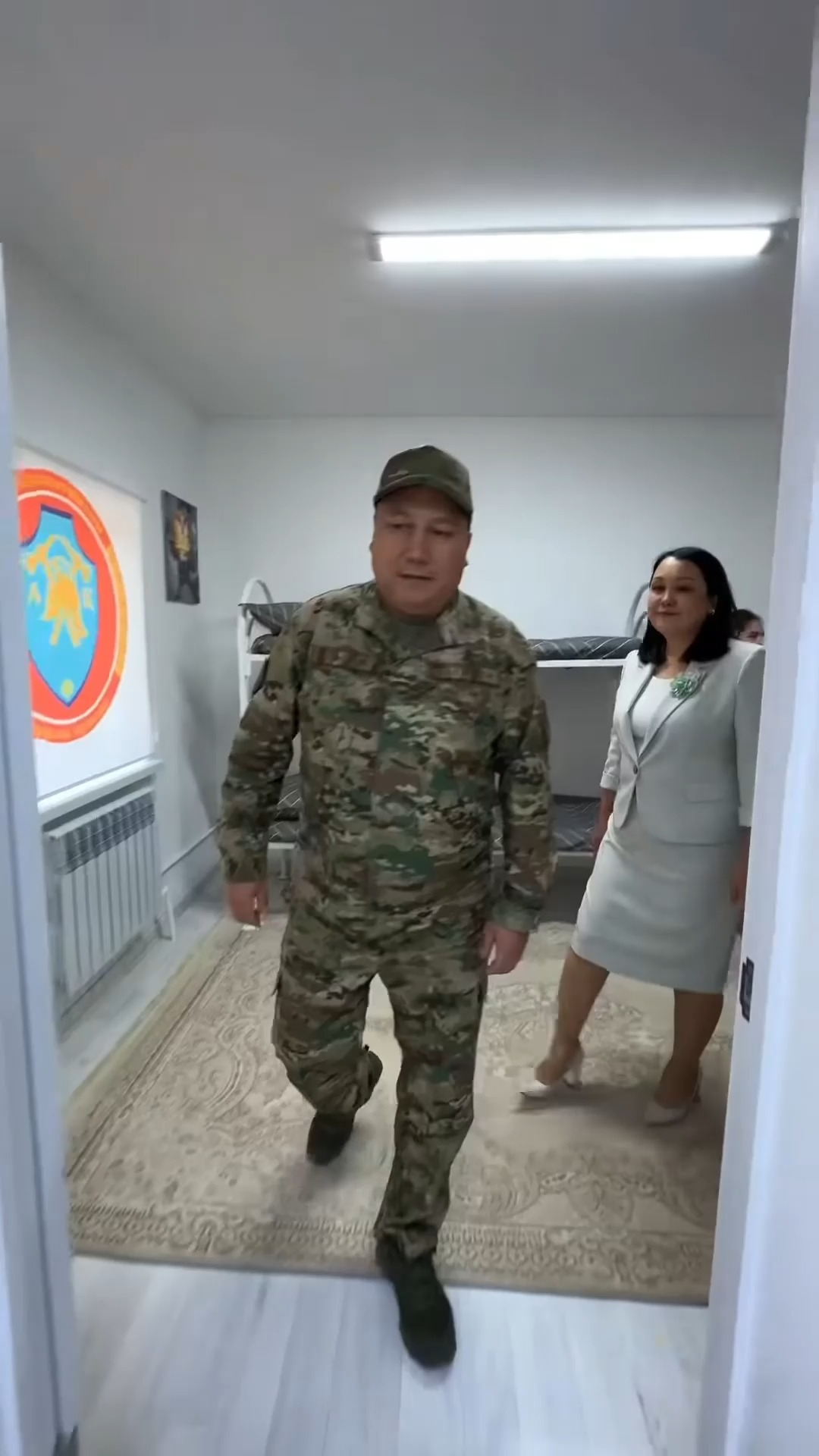 Әскери формадағы ер адам мен костюм киген әйелдің бөлме ішіндегі жүрісі.