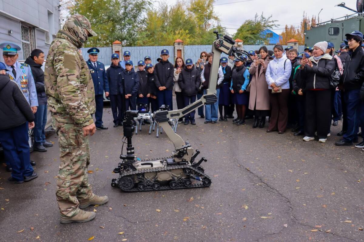 Әскери формадағы адам мен топтың алдында тұрған робот-манипулятор.
