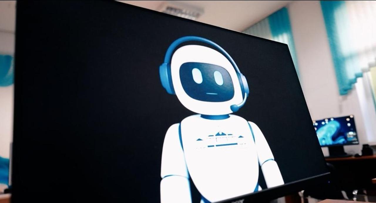 Монитор экранындағы құлаққап таққан робот бейнесі.
