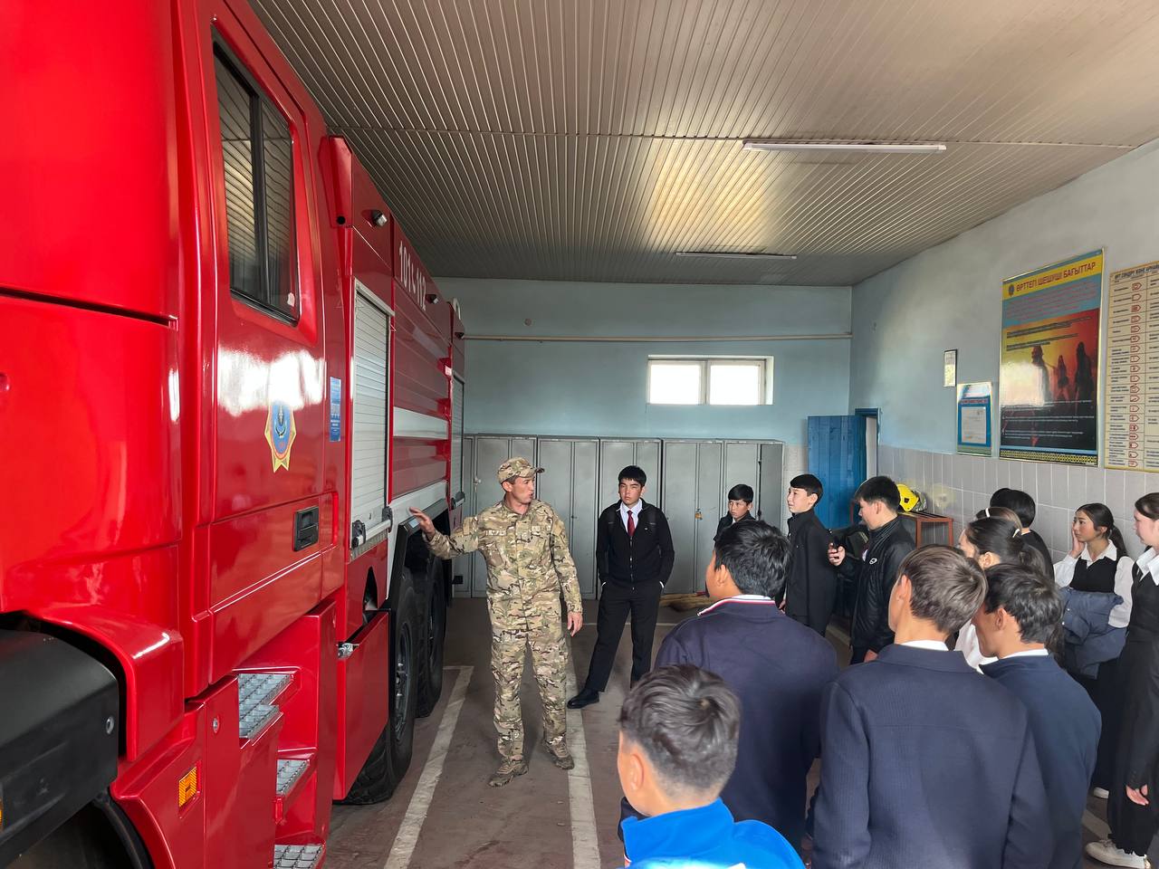 Военный в камуфляже рассказывает группе студентов о пожарной машине в гараже.