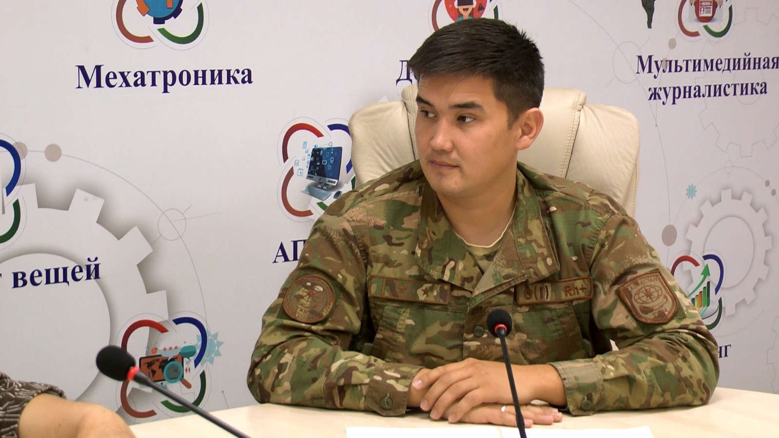 Әскери формадағы ер адам баспасөз мәслихатында отыр.