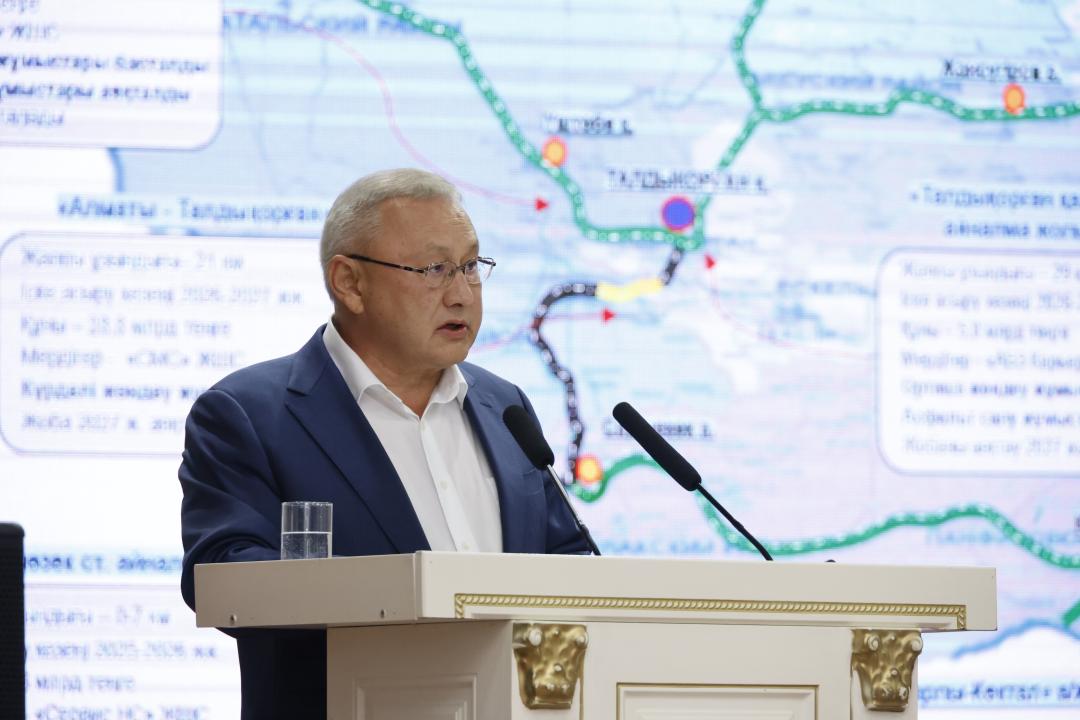 Трибунада картаның алдында сөйлеп тұрған көзілдірікті ер адам.