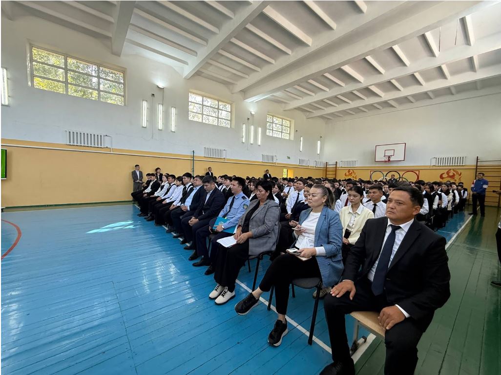 Группа людей в деловой одежде сидит в спортивном зале на мероприятии.