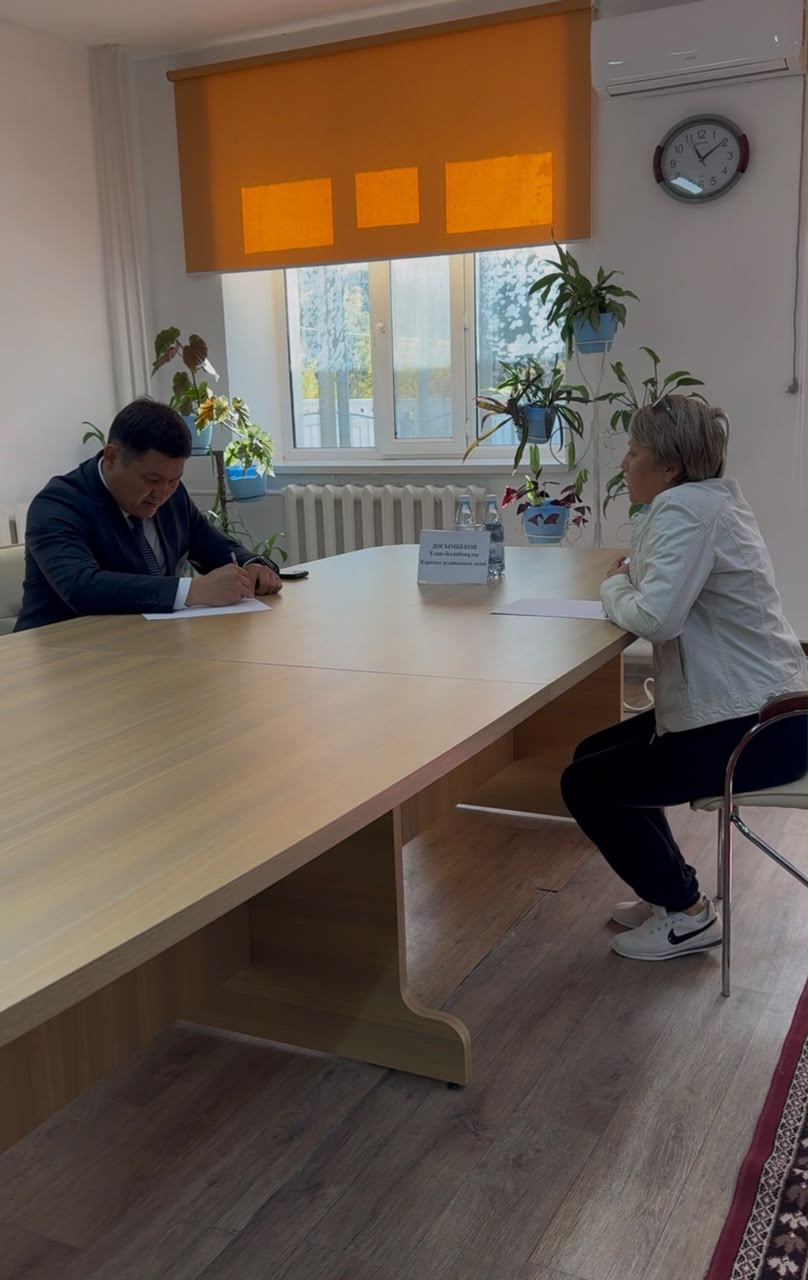 Келіссөз үстелінде отырған екі адам. Ер адам құжатқа қол қойып жатыр.