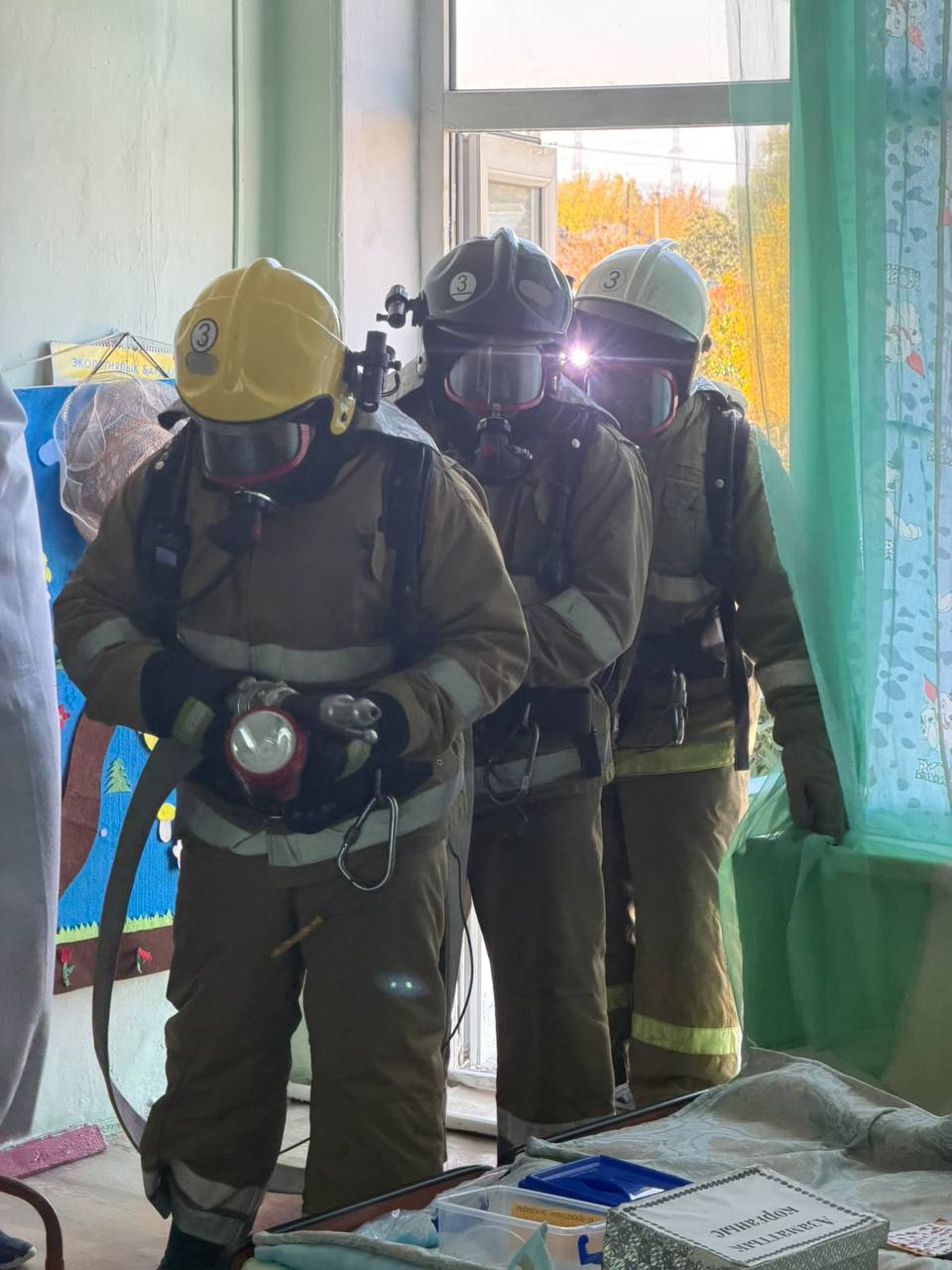 Арнайы киімі мен тыныс алу аппараты бар үш өрт сөндірушінің бөлме ішіндегі бейнесі.