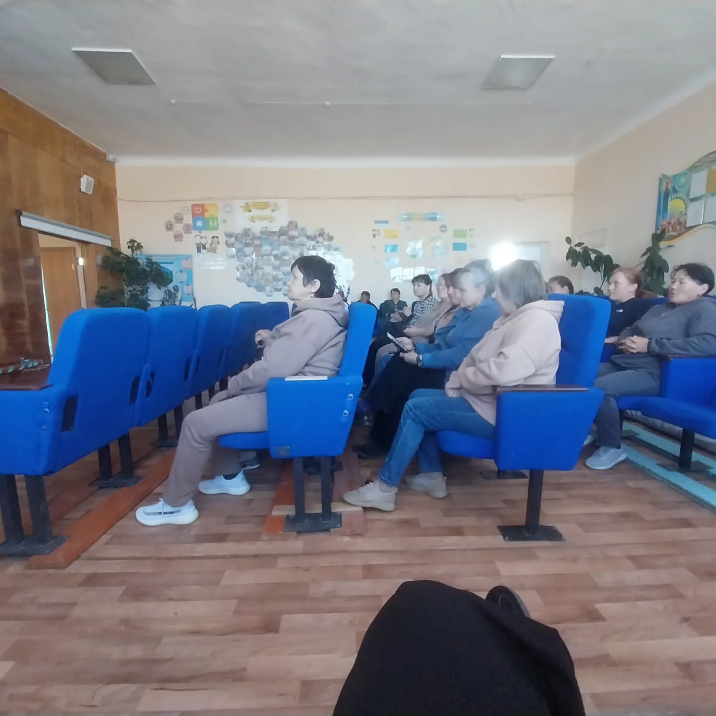 Көк орындықтарда отырған адамдар тобы.