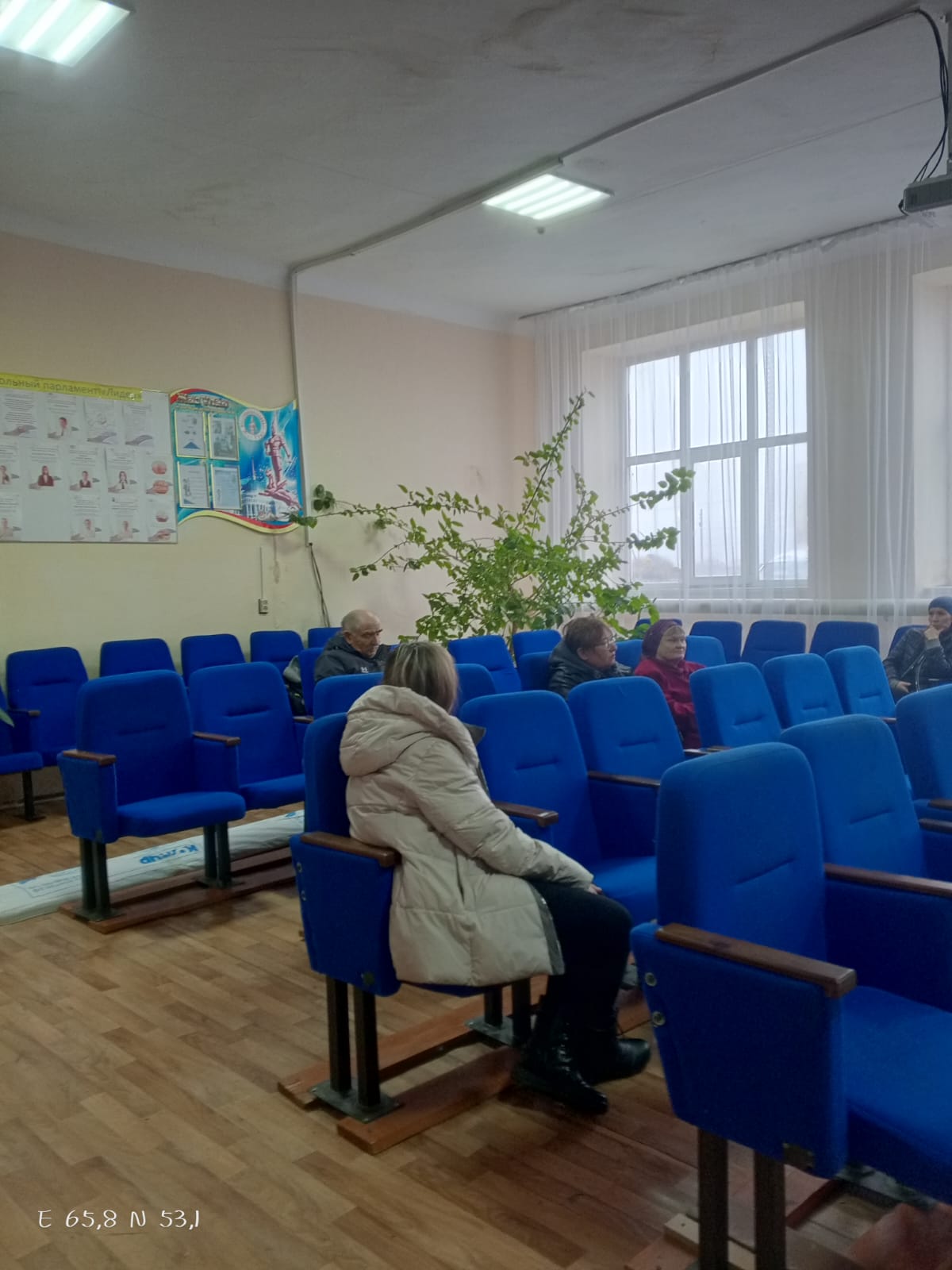 Көк орындықтары бар аудиторияда отырған адамдар.