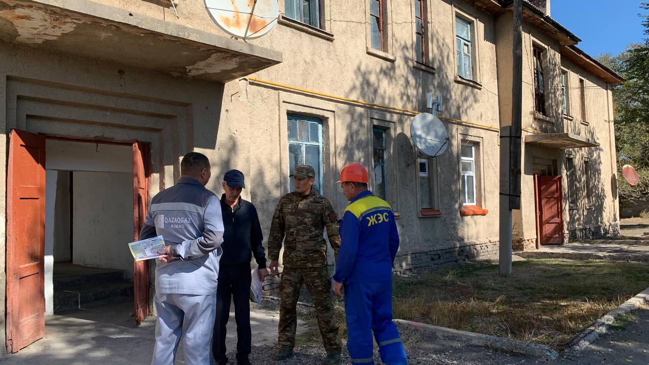 Ескі ғимарат алдында тұрған әкімшілік қызметкерлер, әскери және арнайы киімдегі мамандар тобы.