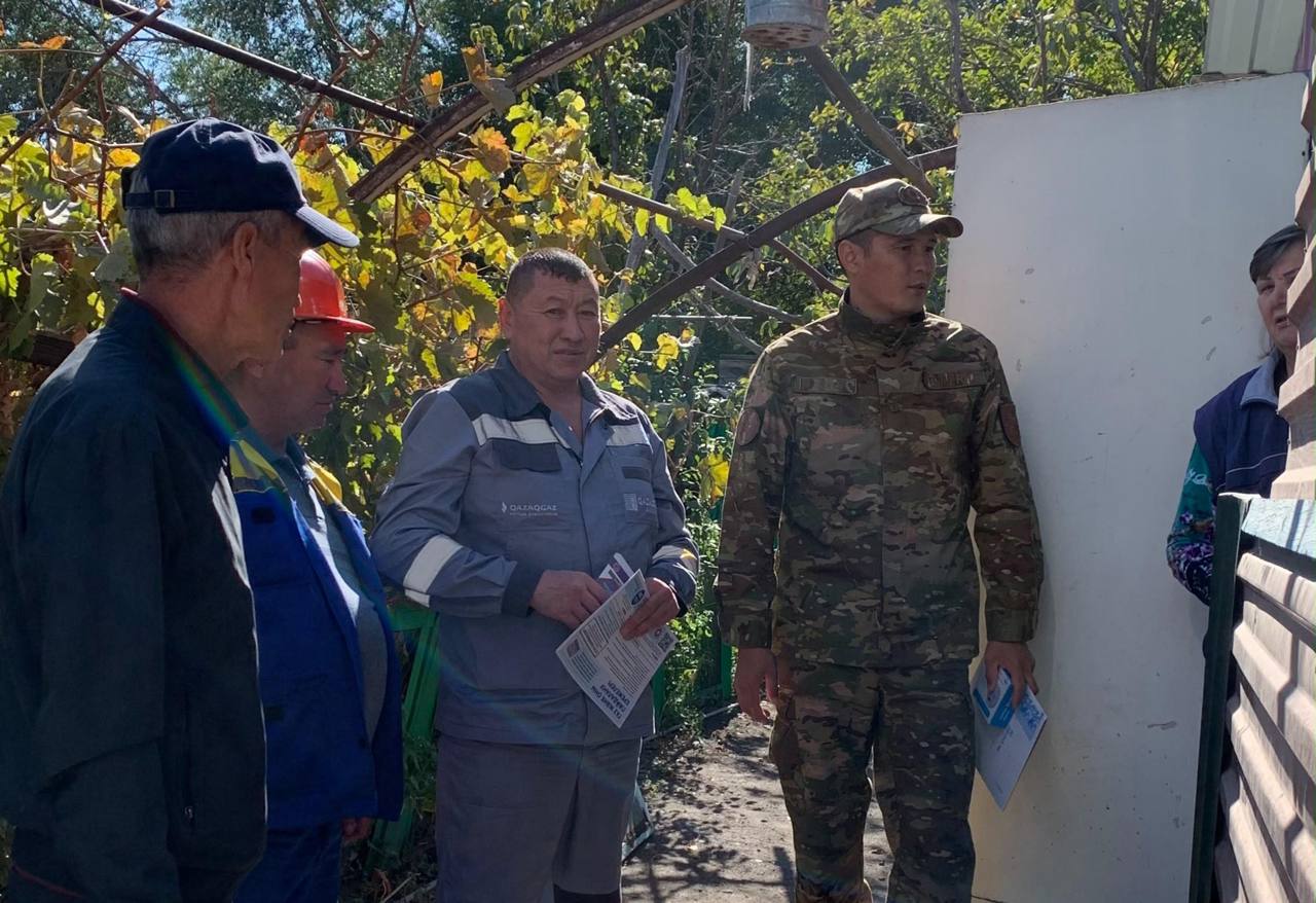 Ауылдағы үйдің жанында әңгімелесіп тұрған әскери қызметші, арнайы киімдегі маман және жергілікті тұрғындар.