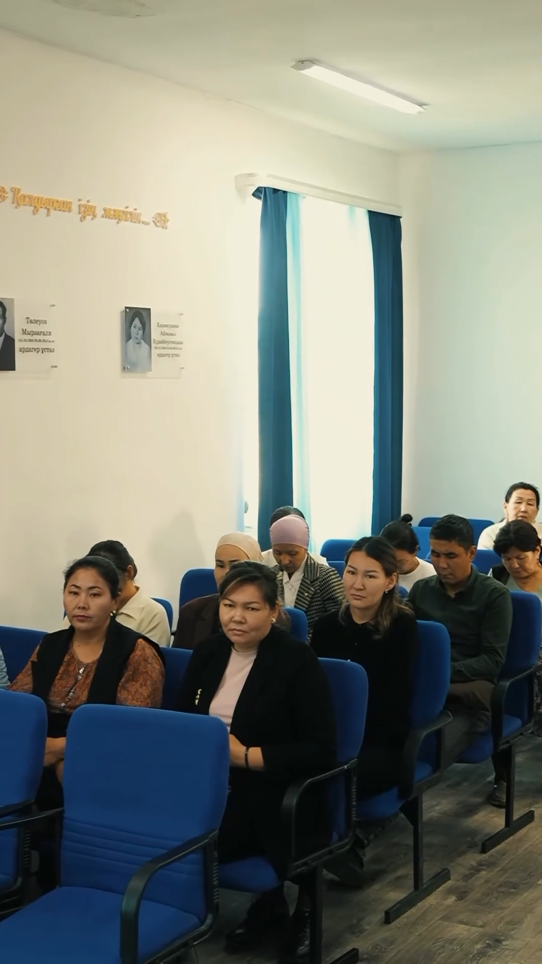 Көк орындықтарда отырған адамдар тобы.