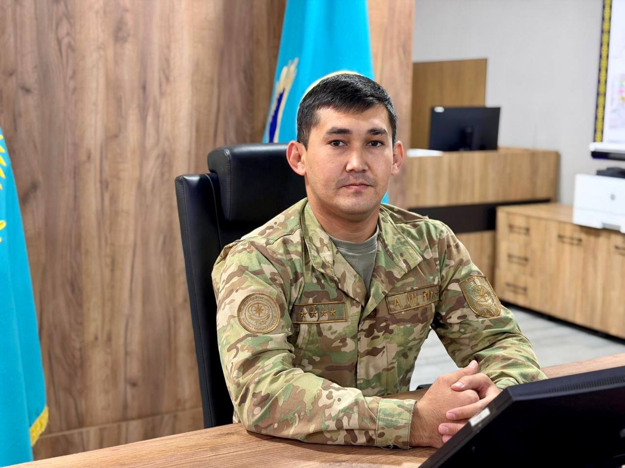 Камуфляж киген әскери қызметші кеңседе үстел басында отыр.