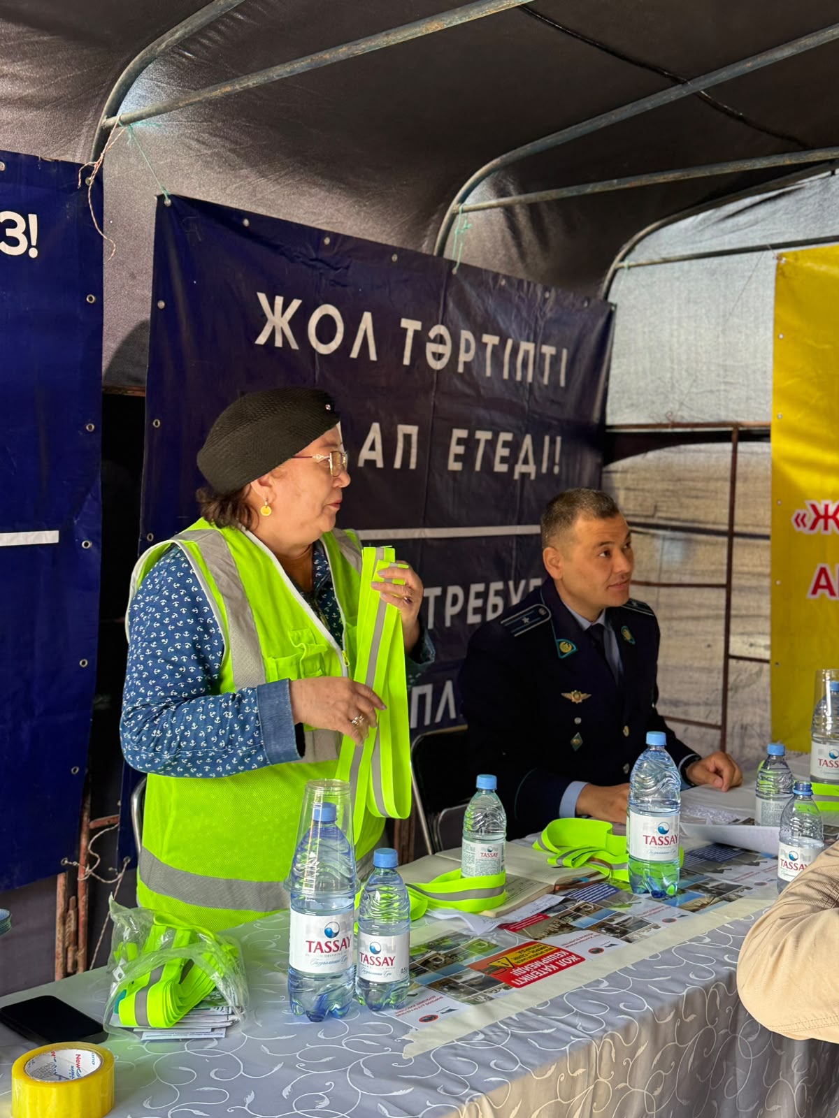 Жол тәртібі туралы ақпараттық шарада сөйлеп тұрған әйел және полиция қызметкері.