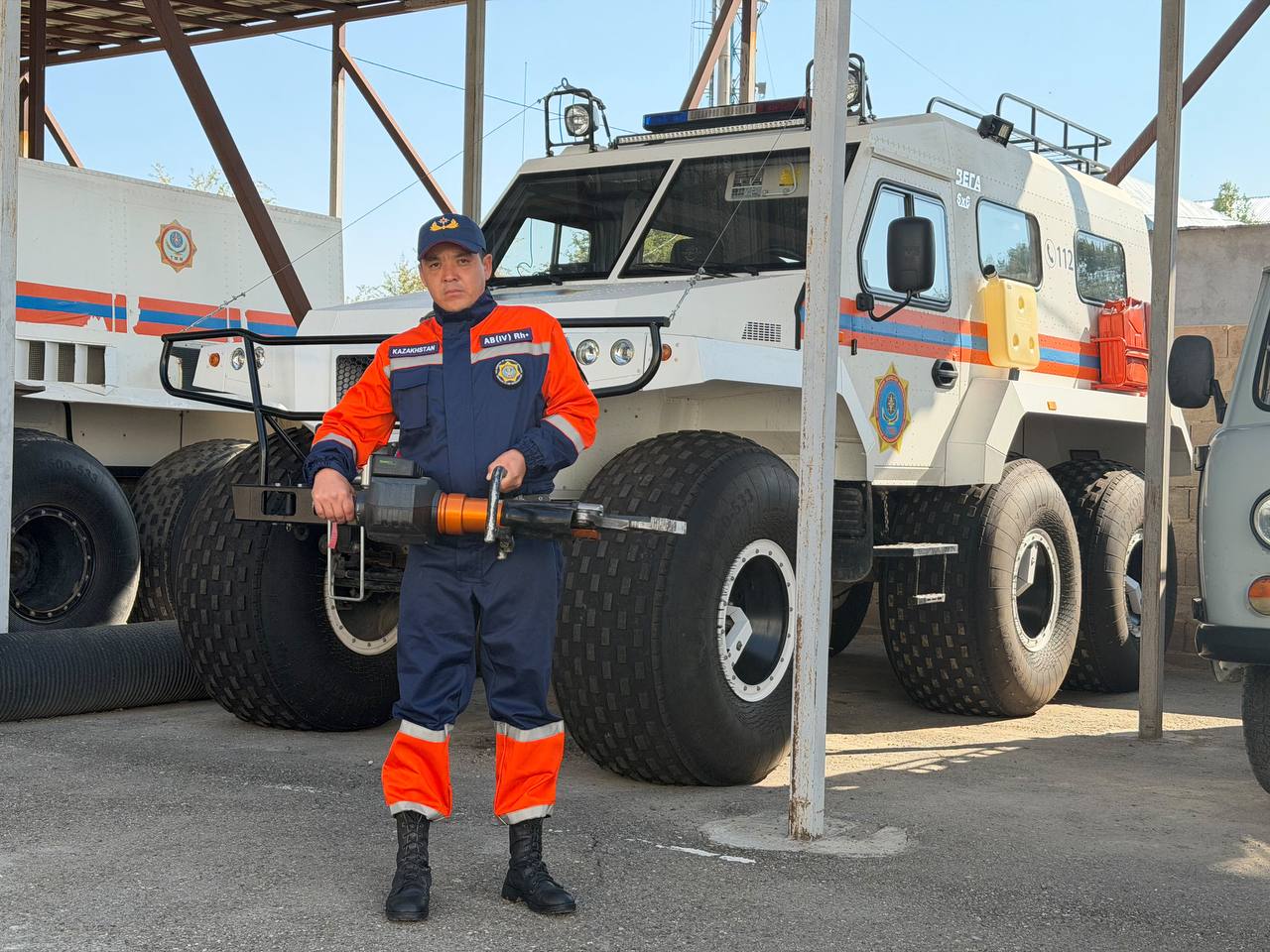 Өрт сөндіруші маманы арнайы техниканың жанында құрал ұстап тұр.