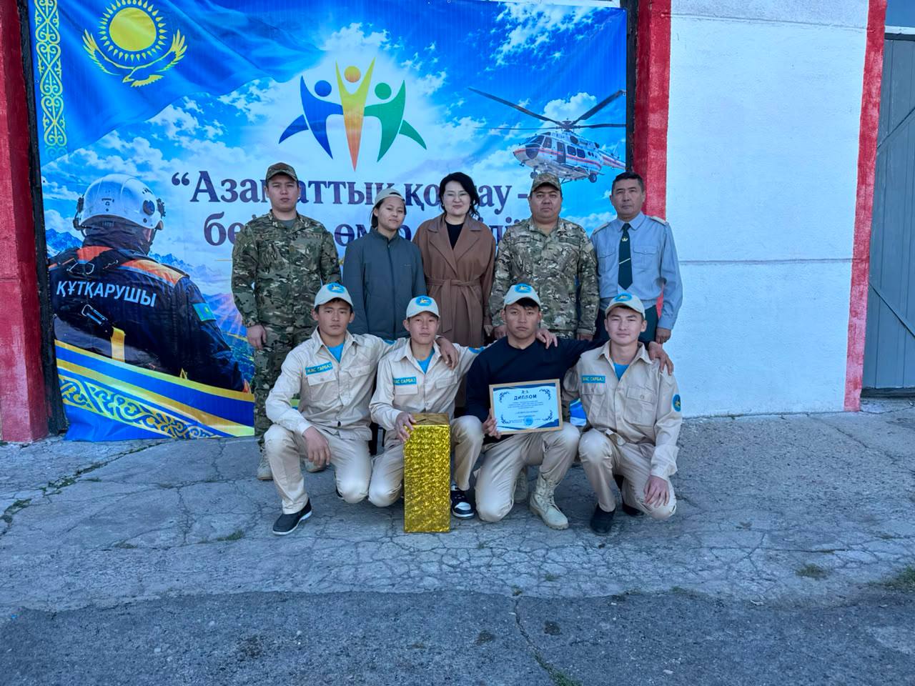 Құтқарушылар мен ұйымдастырушылардың баннер алдындағы топтық суреті.