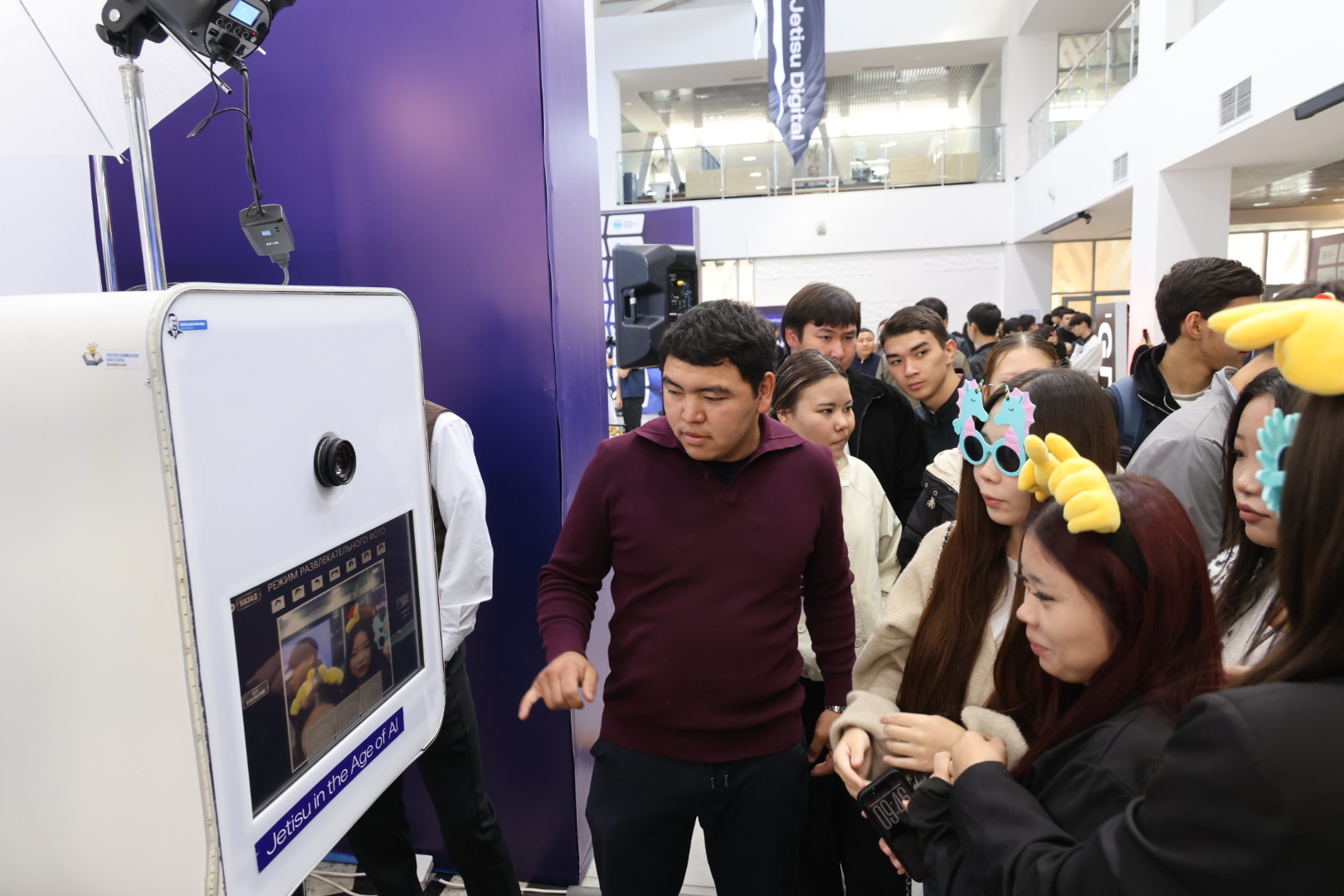 Группа молодых людей у интерактивного фотокиоска с надписью «Jetisu in the Age of AI» на мероприятии.